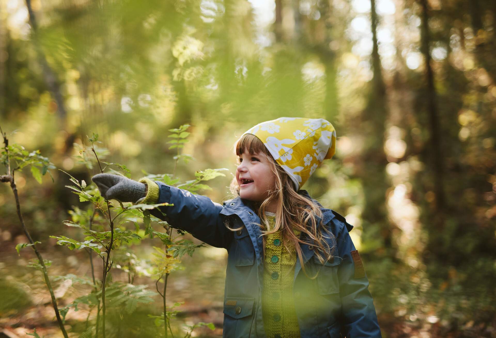 A little girl dressed in warm clothing pointing at a plant during forest hike.
