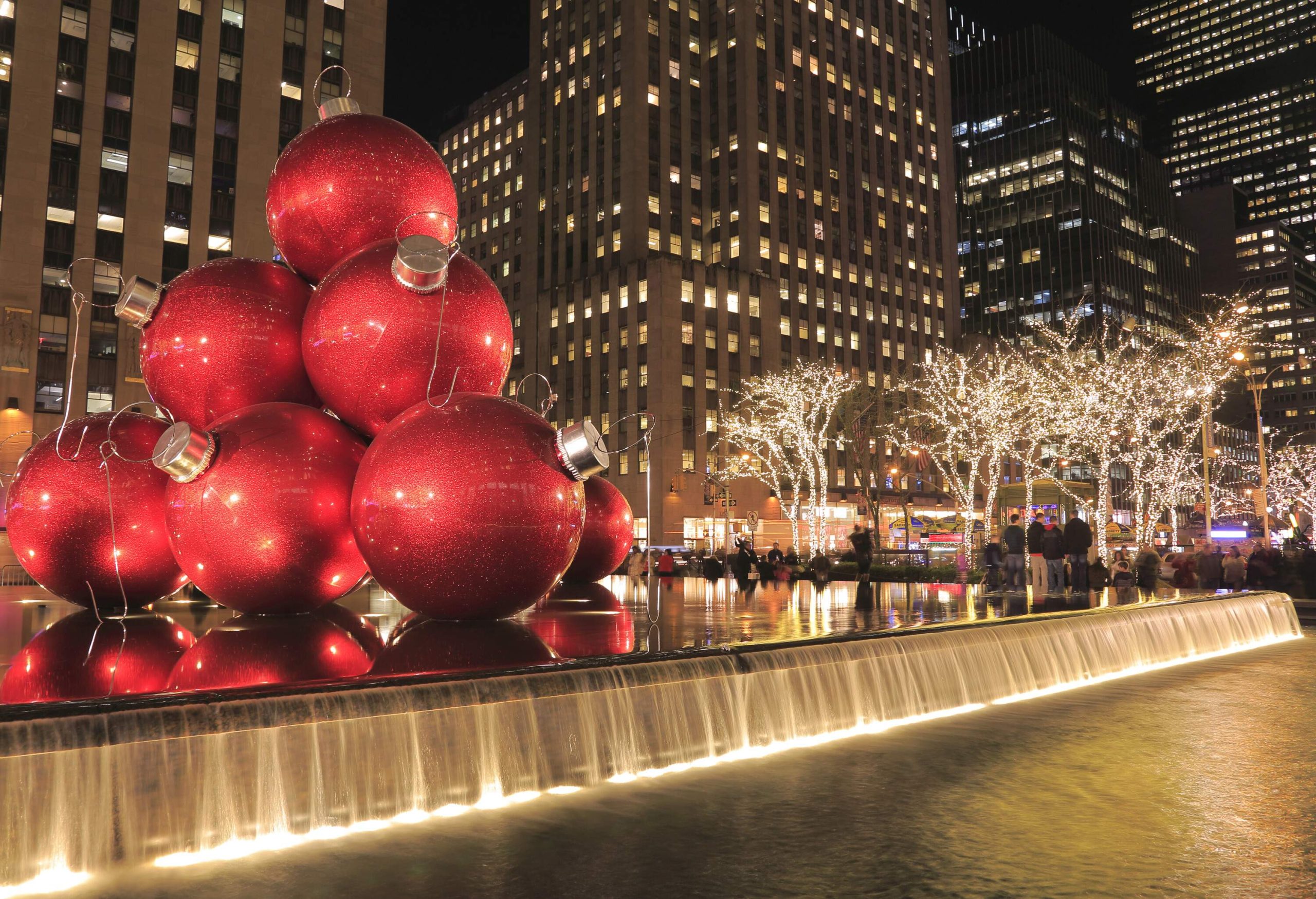 Giant red Christmas balls on top of the fountain surrounded by the tall building.