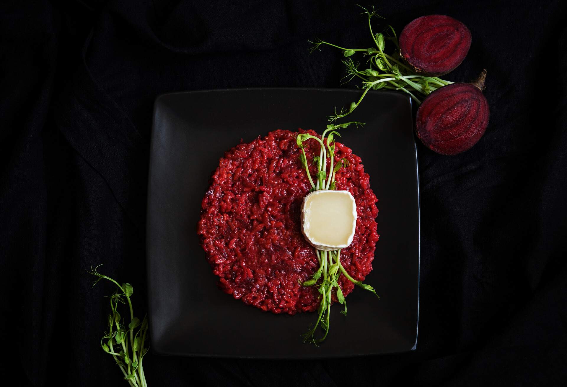 Tasty beetroot risotto with goat cheese and sprouts on a black plate. Culinary eating.