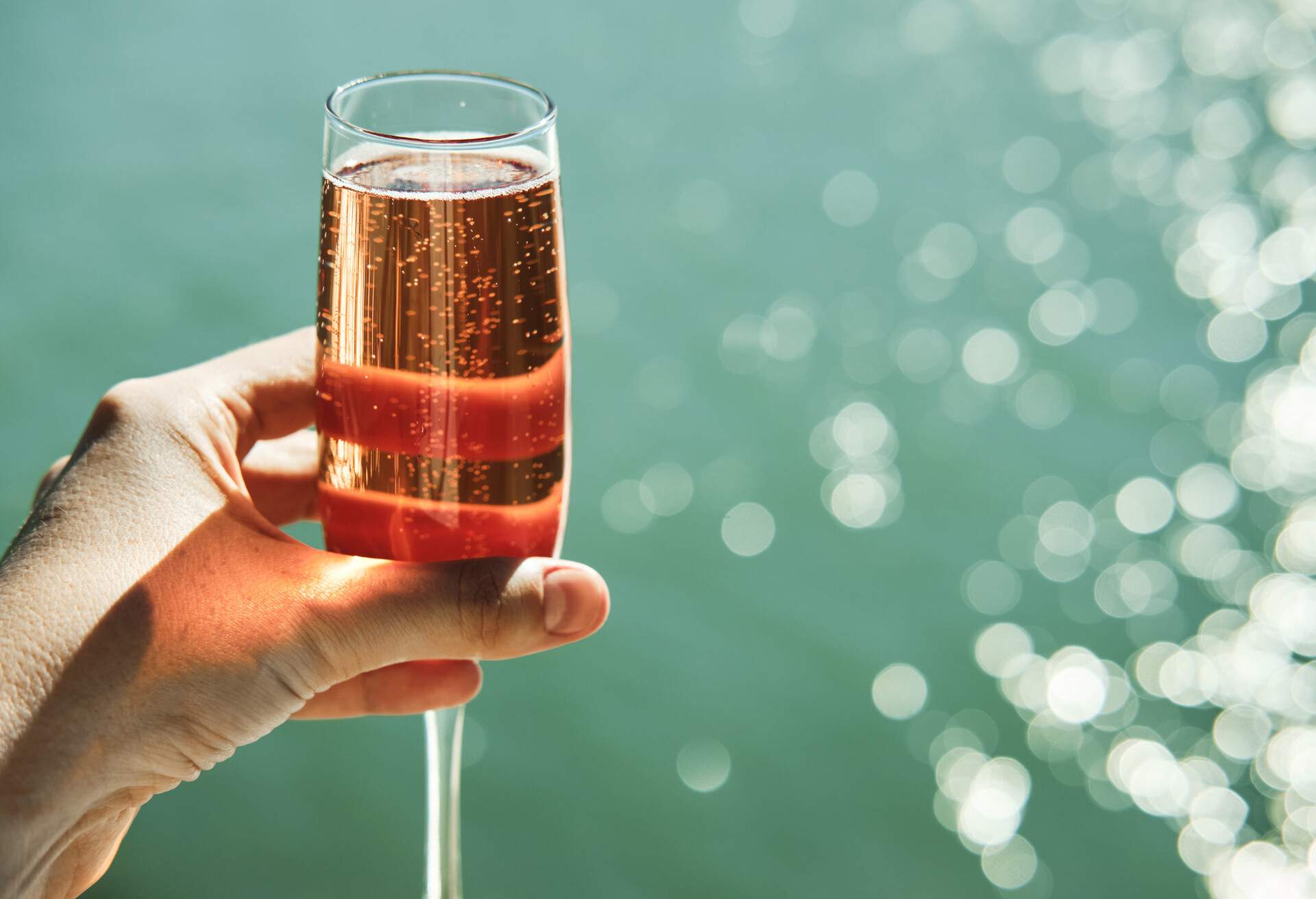Glass of pink champagne in woman's hand in front of the lake on a sunny summer day