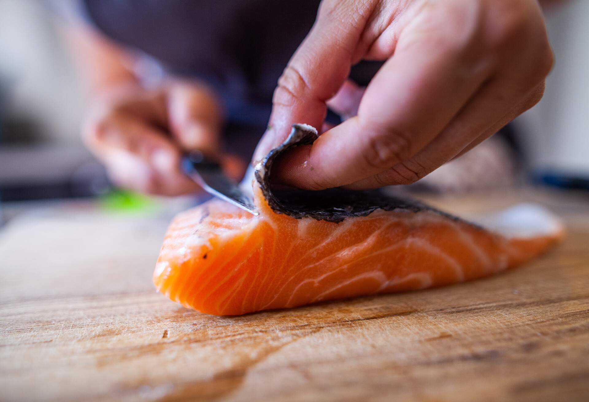 Cette photographie présente en cuisine une personne en train de découper du poisson, notamment du saumon, un pavé.