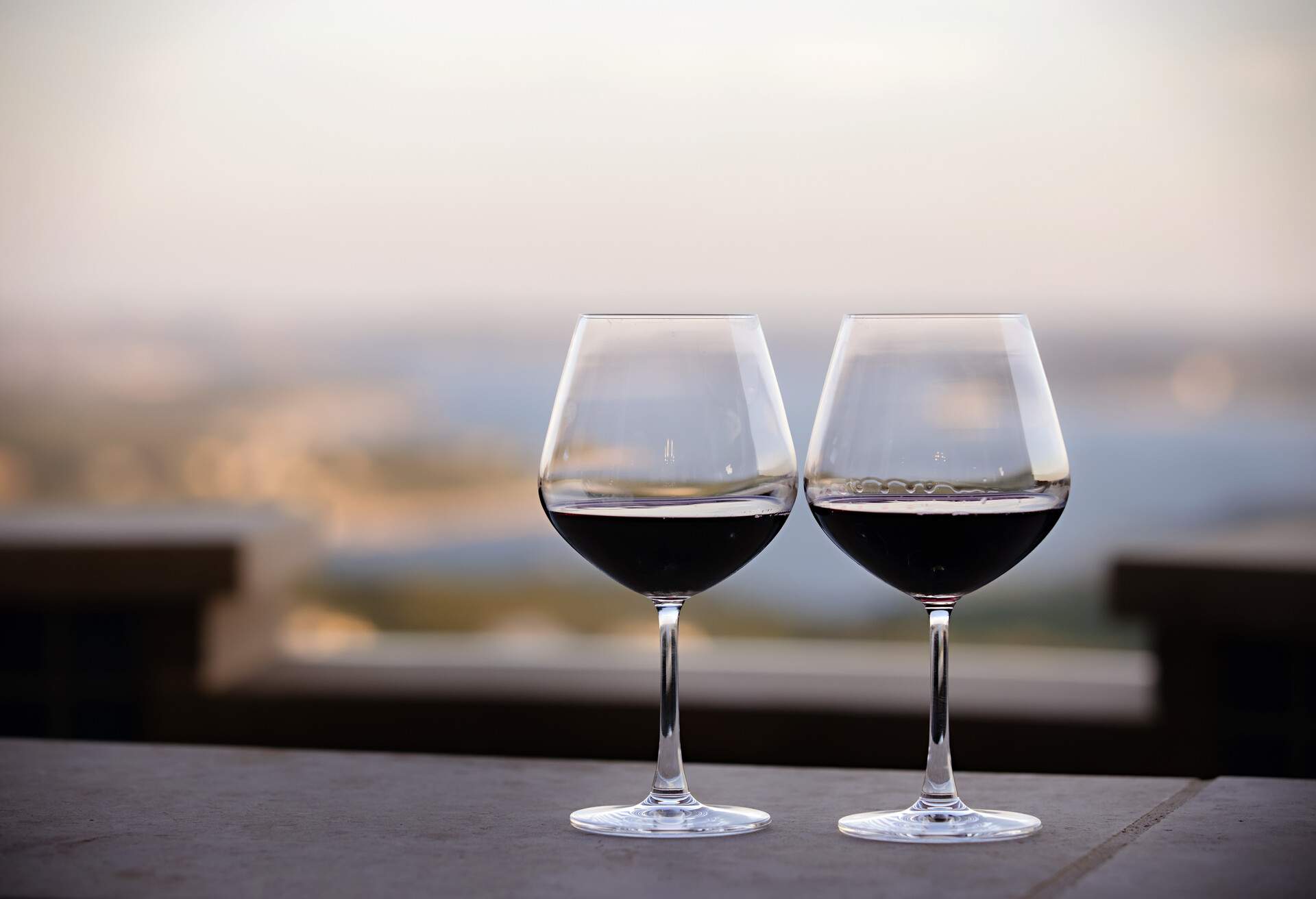 Two Red Wine Glasses side by side on a table with a view overlooking a lake