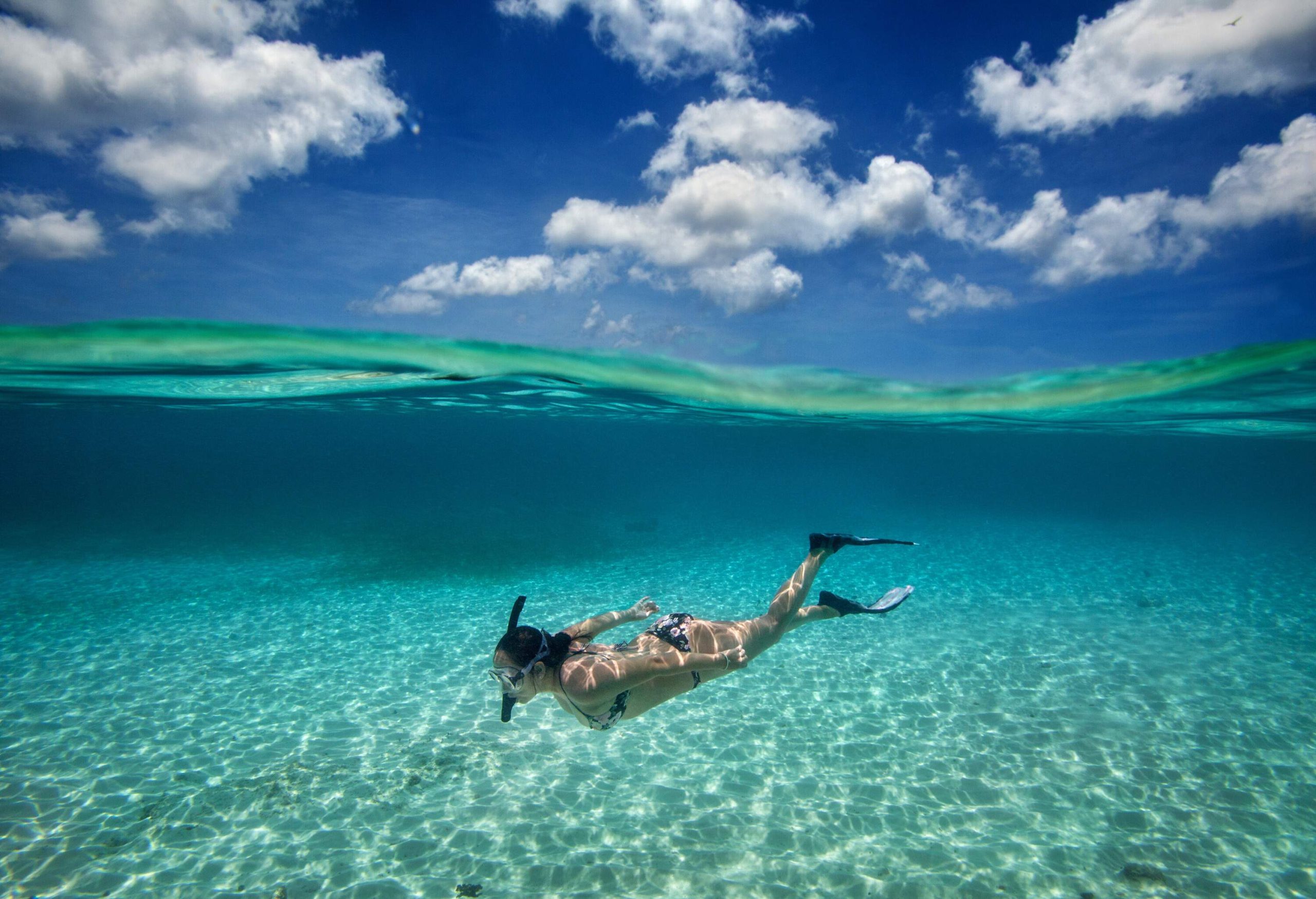 A woman snorkelling in a clear sea as the sunlight reflects off the sandy bottom.