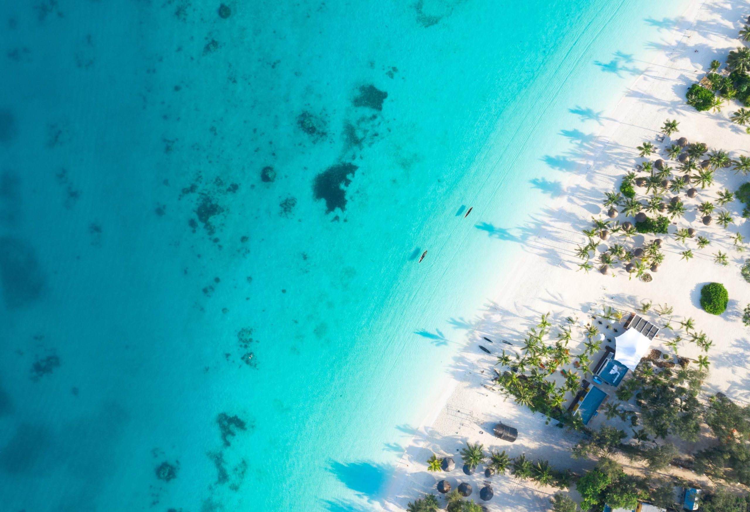 Top view of a turquoise water sea with a fine white sand shore.