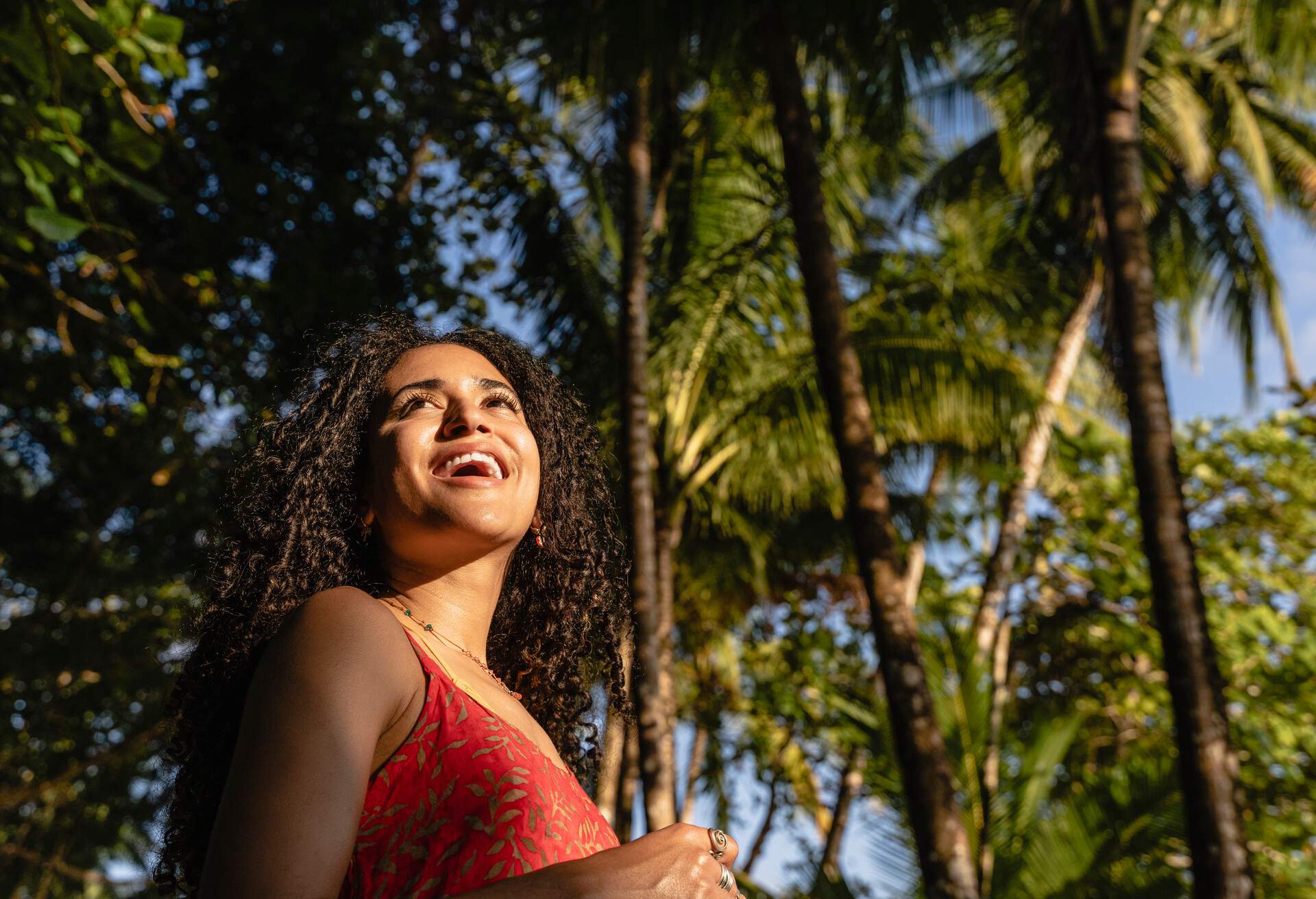 Portrait with copy space of a smiling woman looking ahead next to palm trees in a sunny day