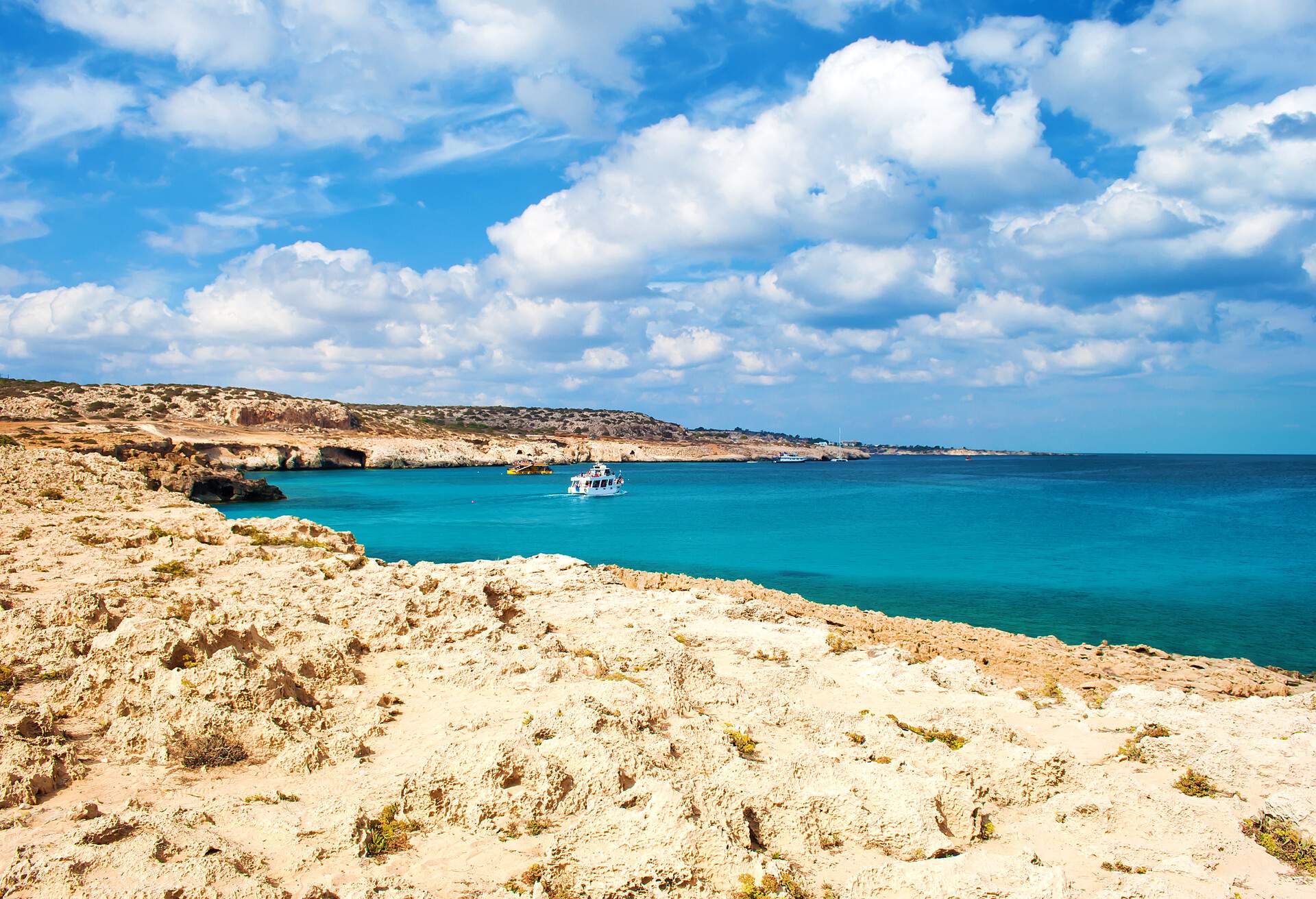 View of the Blue Lagoon bay near Cape Greco, Cyprus. Rock coastline near deep green transparent azure water, one white boat. Amazing cloudscape. Warm day in fall