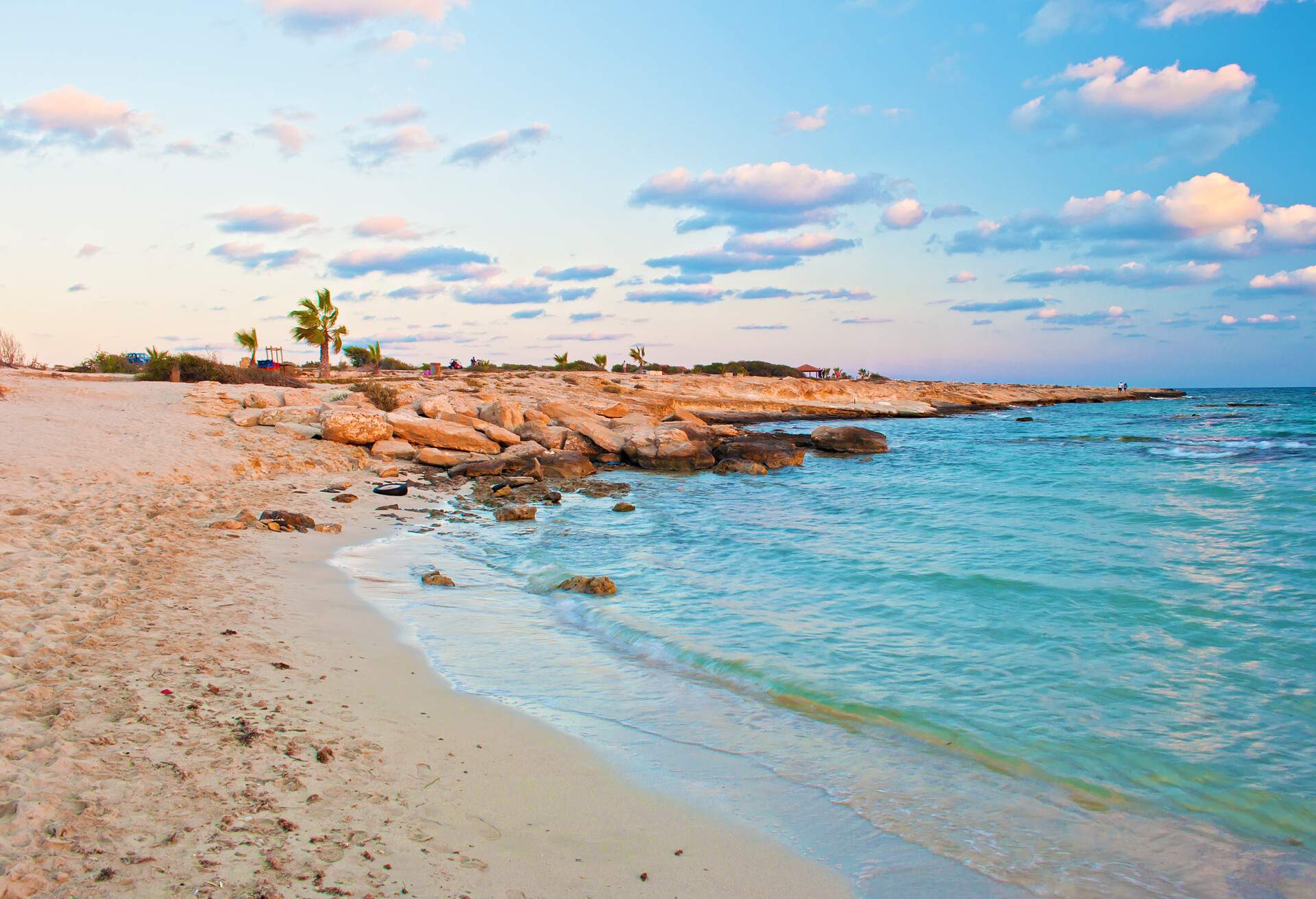 Image of breathtaking Landa beach in Agia Napa, Cyprus. Yellow sand and boulders against blue calm water with small waves on a warm evening in fall, small clouds in the sky. Shot during golden hour