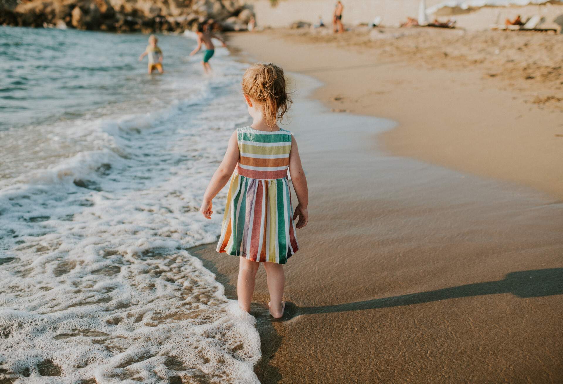 Cute little girl wearing a linen dress, on a beach at sunset.
