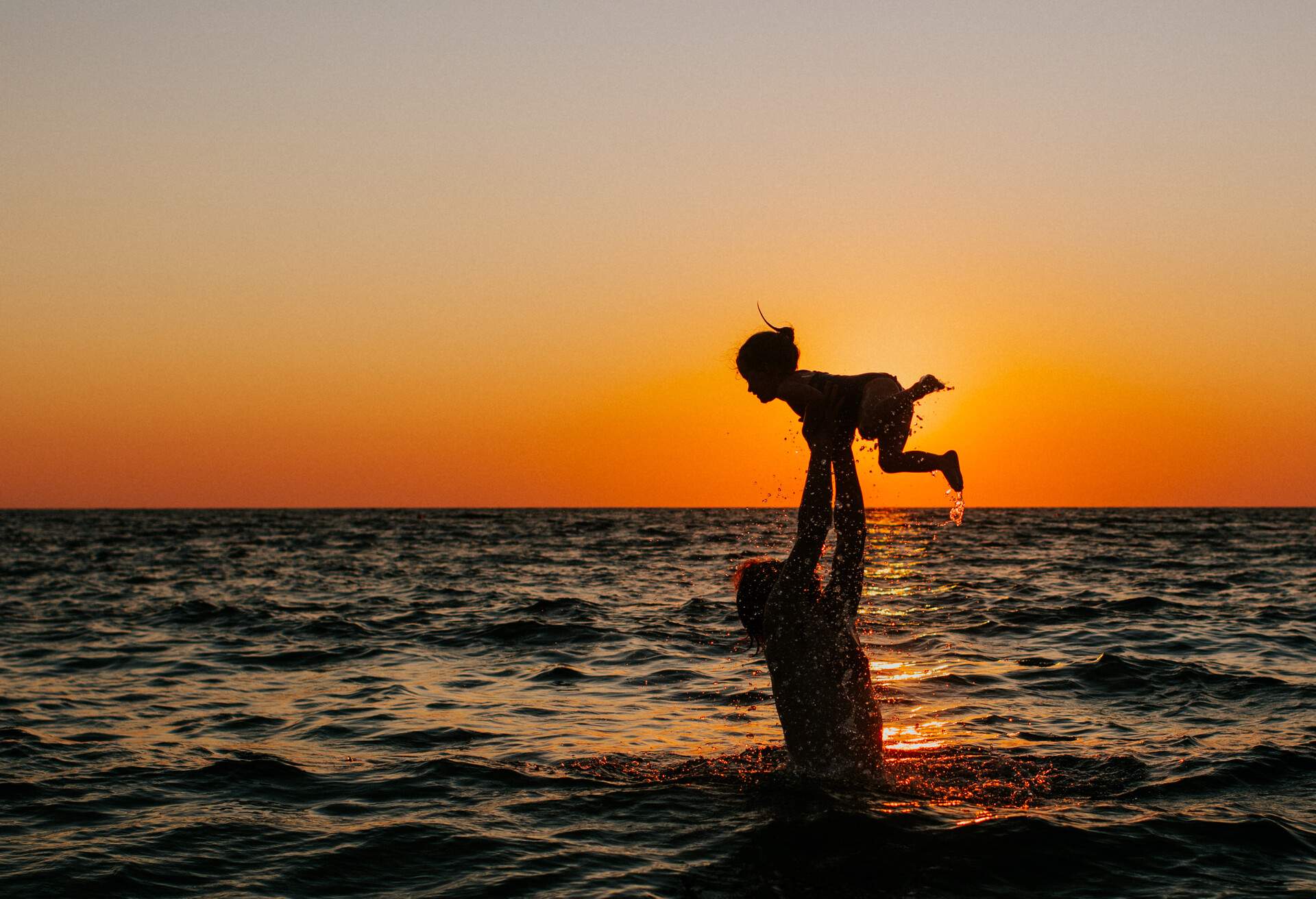 Father and child in the sea at sunset. Father throwing child into the air.