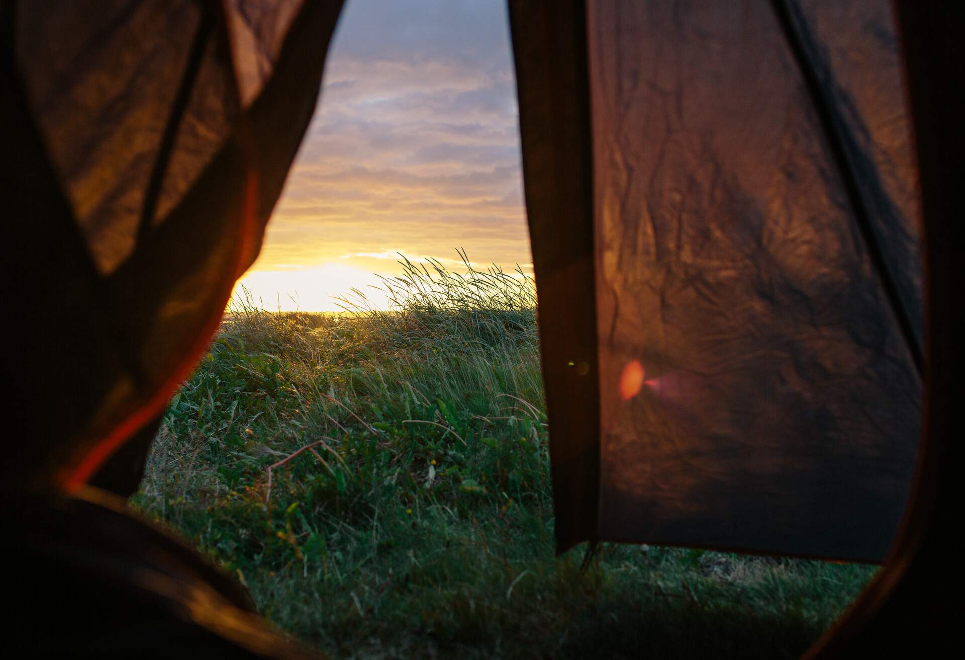 The open door of a tent overlooking the dramatic sunset and Breidaik beach in Iceland's westfjords