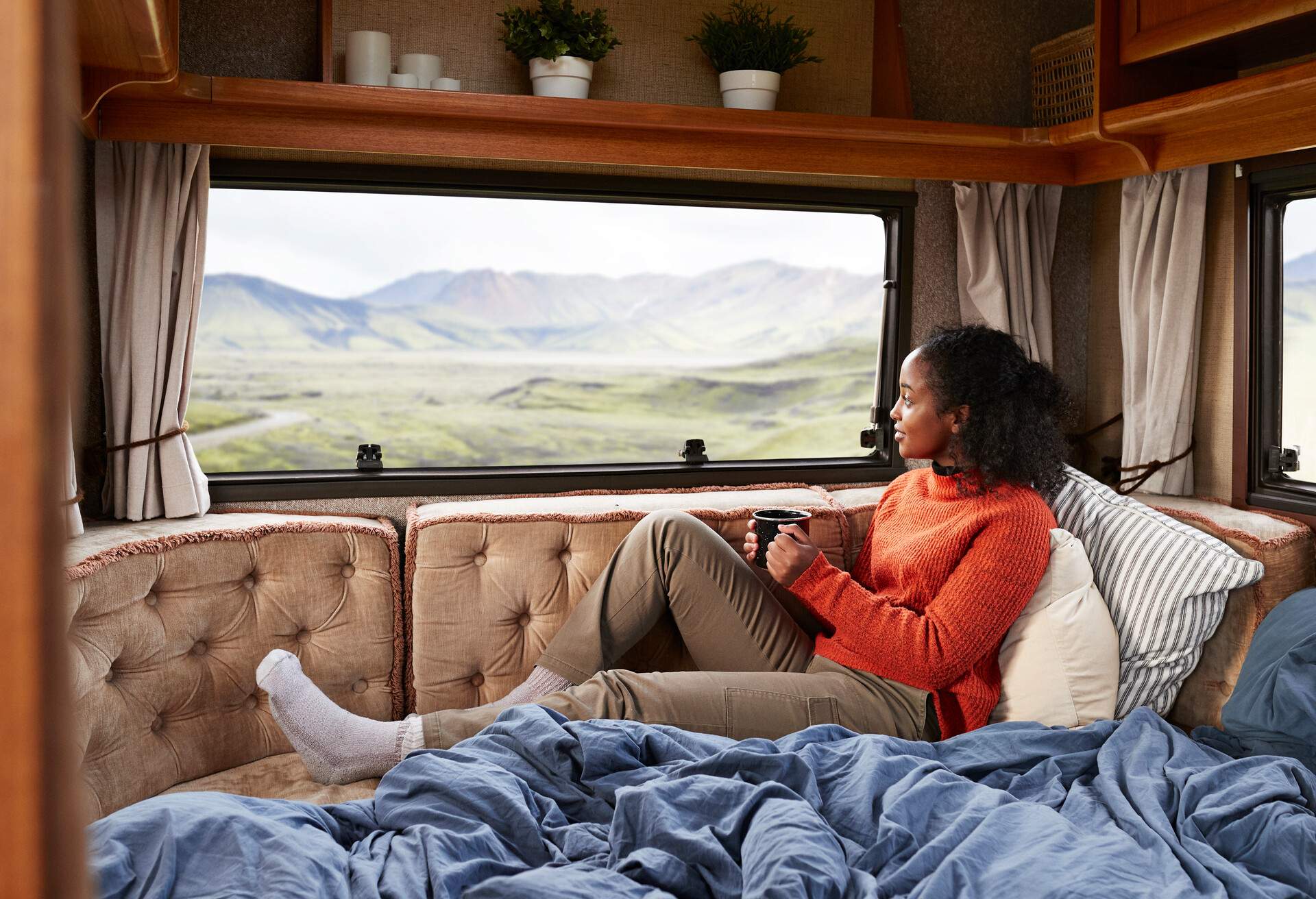 Contemplating woman with coffee cup sitting on bed in camper van