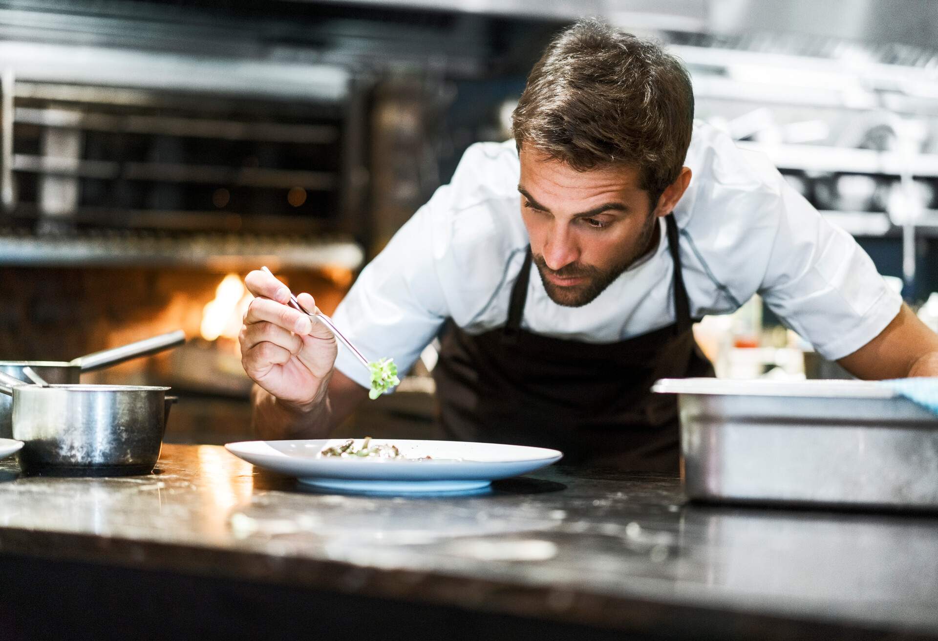 Concentrated chef garnishing food. Male cook is preparing dish in commercial kitchen. He is working in restaurant.