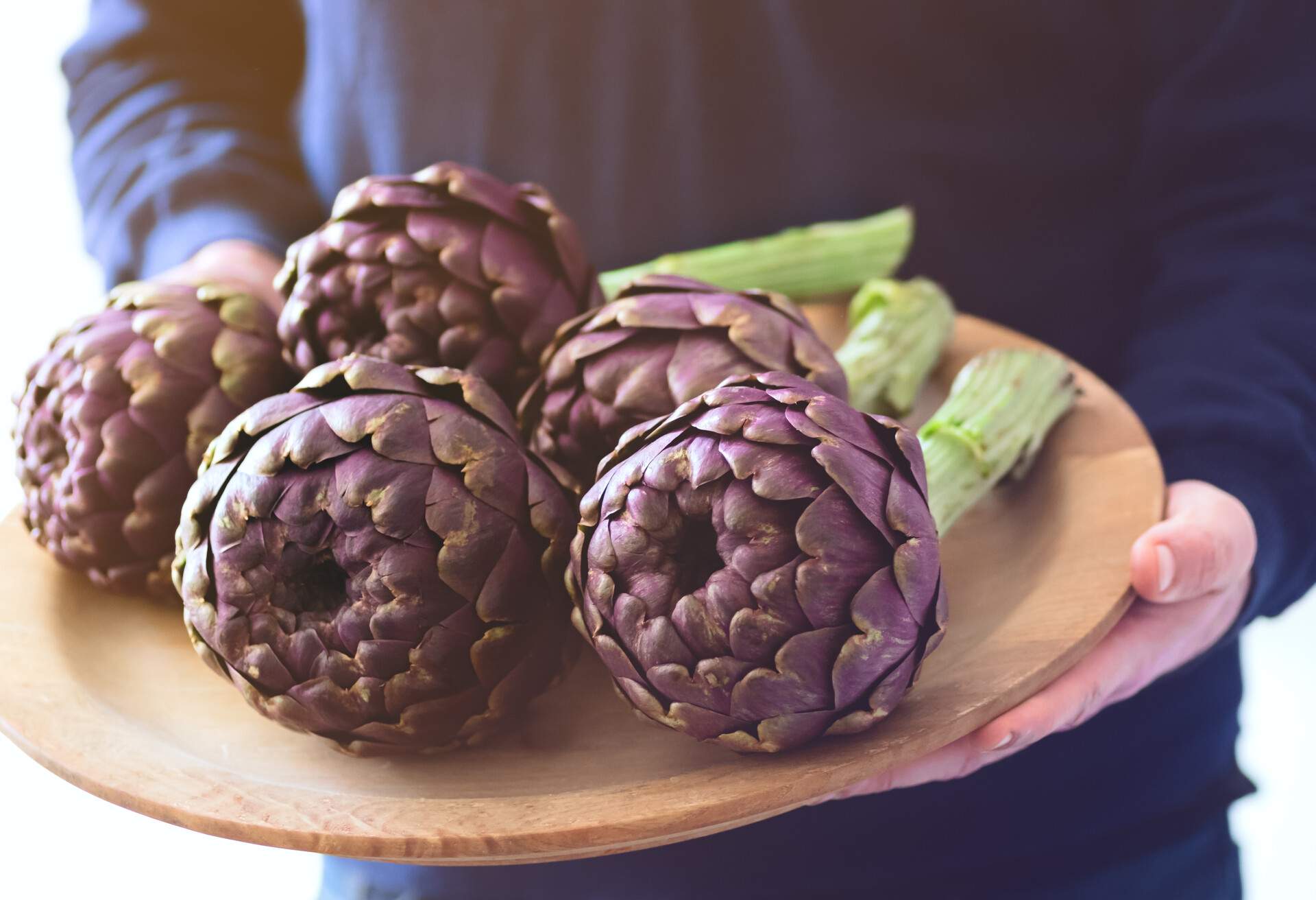 Artichokes. The man is holding a plate with fresh artichokes. Ingredients of southern Italian cuisine 