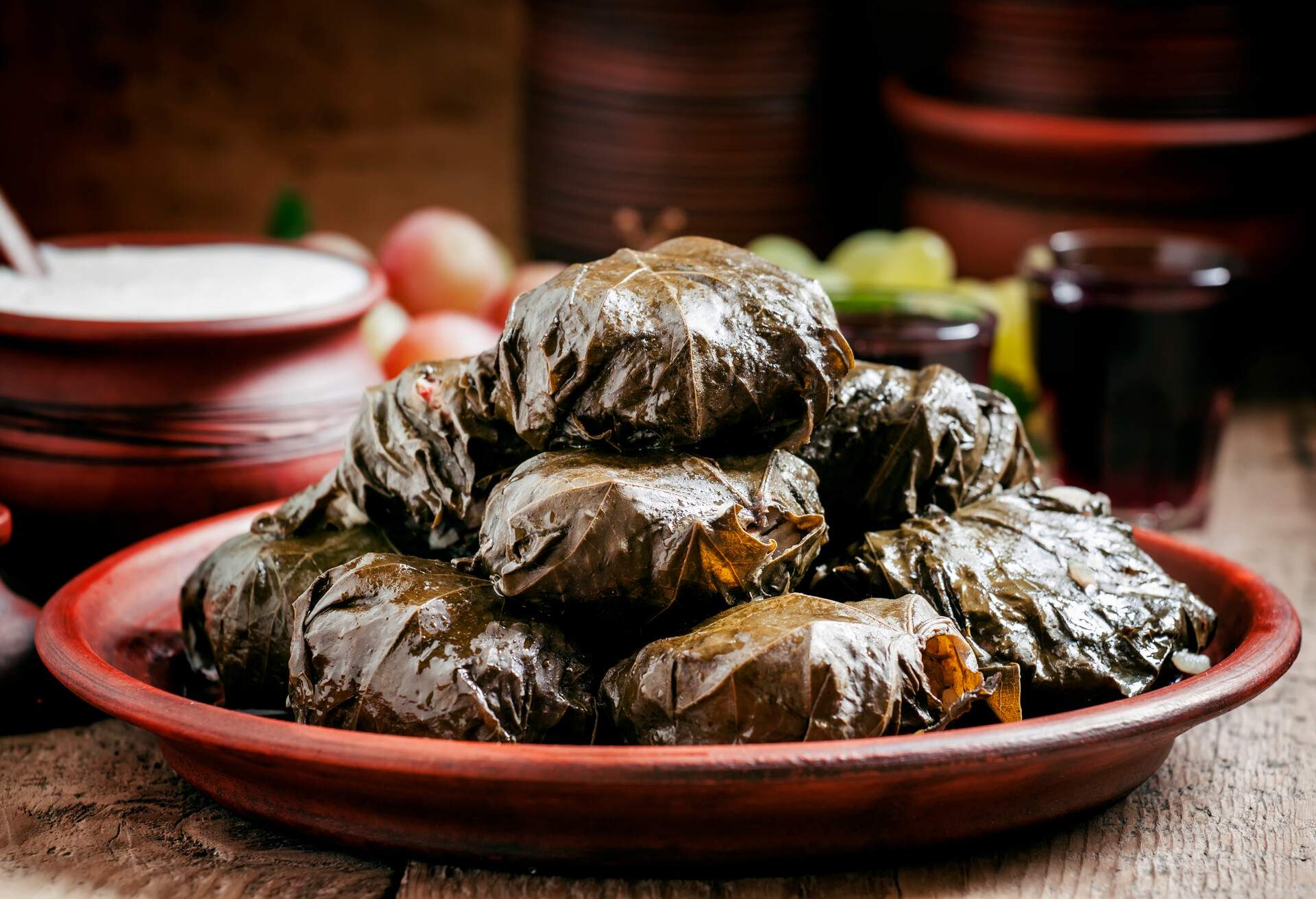 Traditional Greek dolma with meat in grape leaves, yogurt sauce, grapes and red wine on a clay dish, selective focus