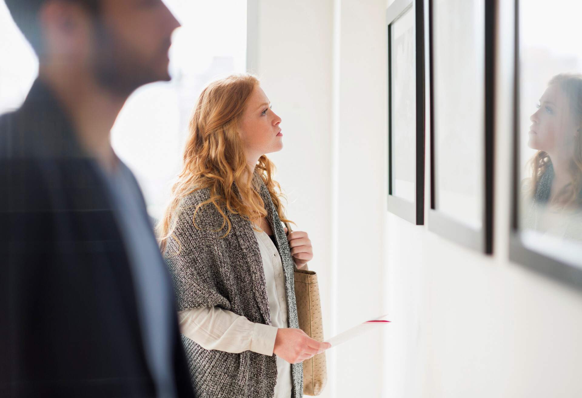 Blonde woman clutching her bag while staring intently at an artwork on a wall.