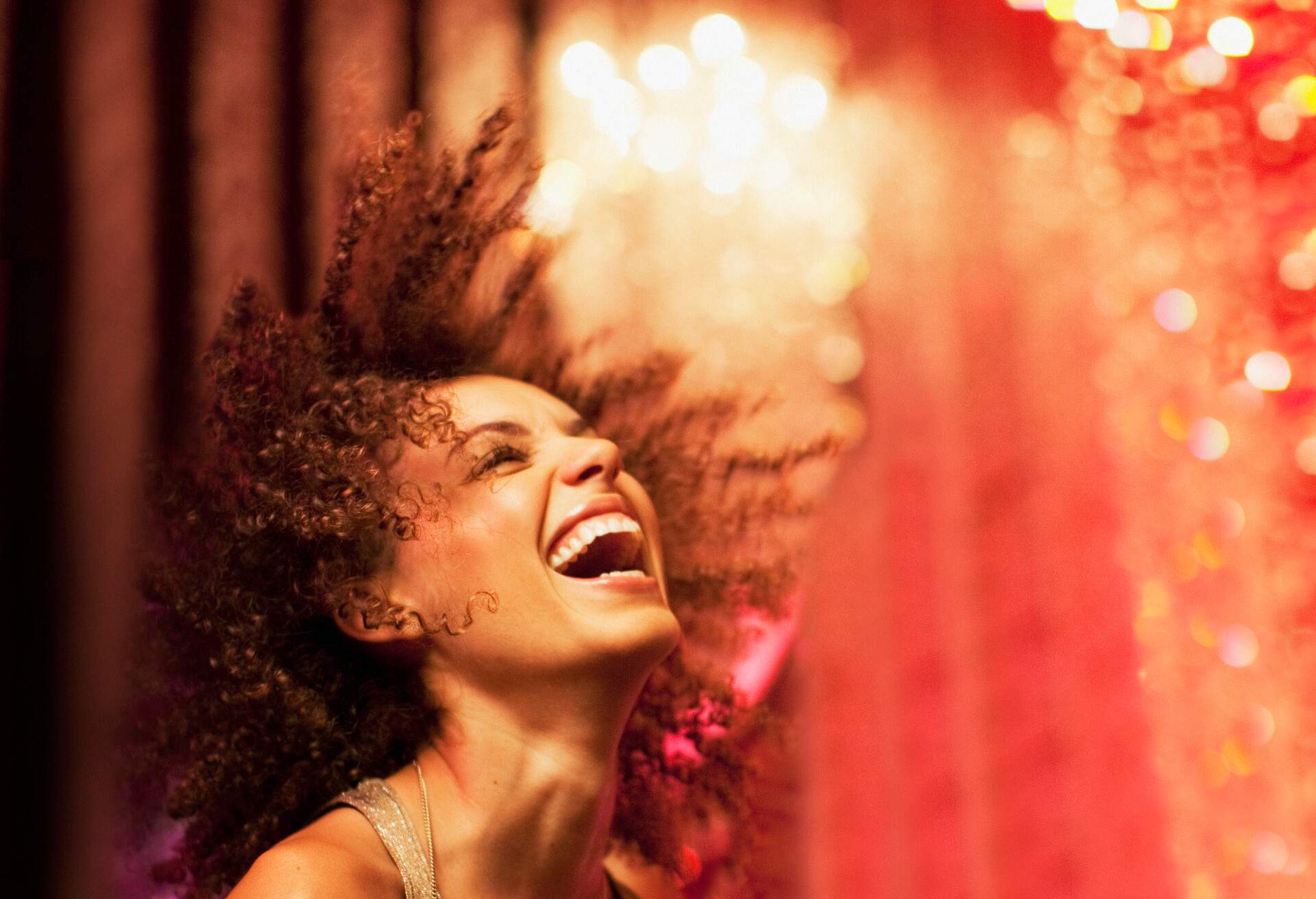 Laughing woman with afro hair with red lights background behind her.