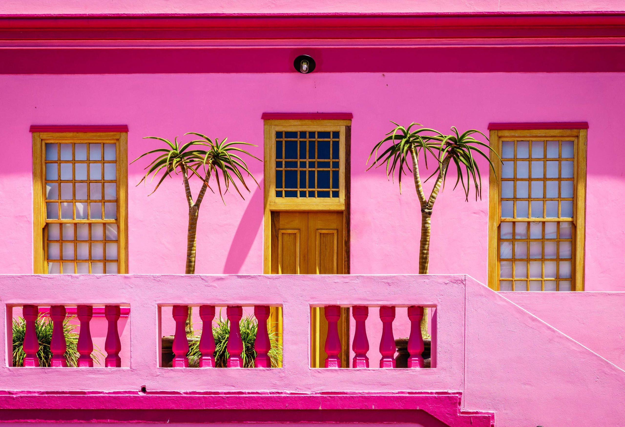 A pink building with wooden windows and a balcony with potted plants.