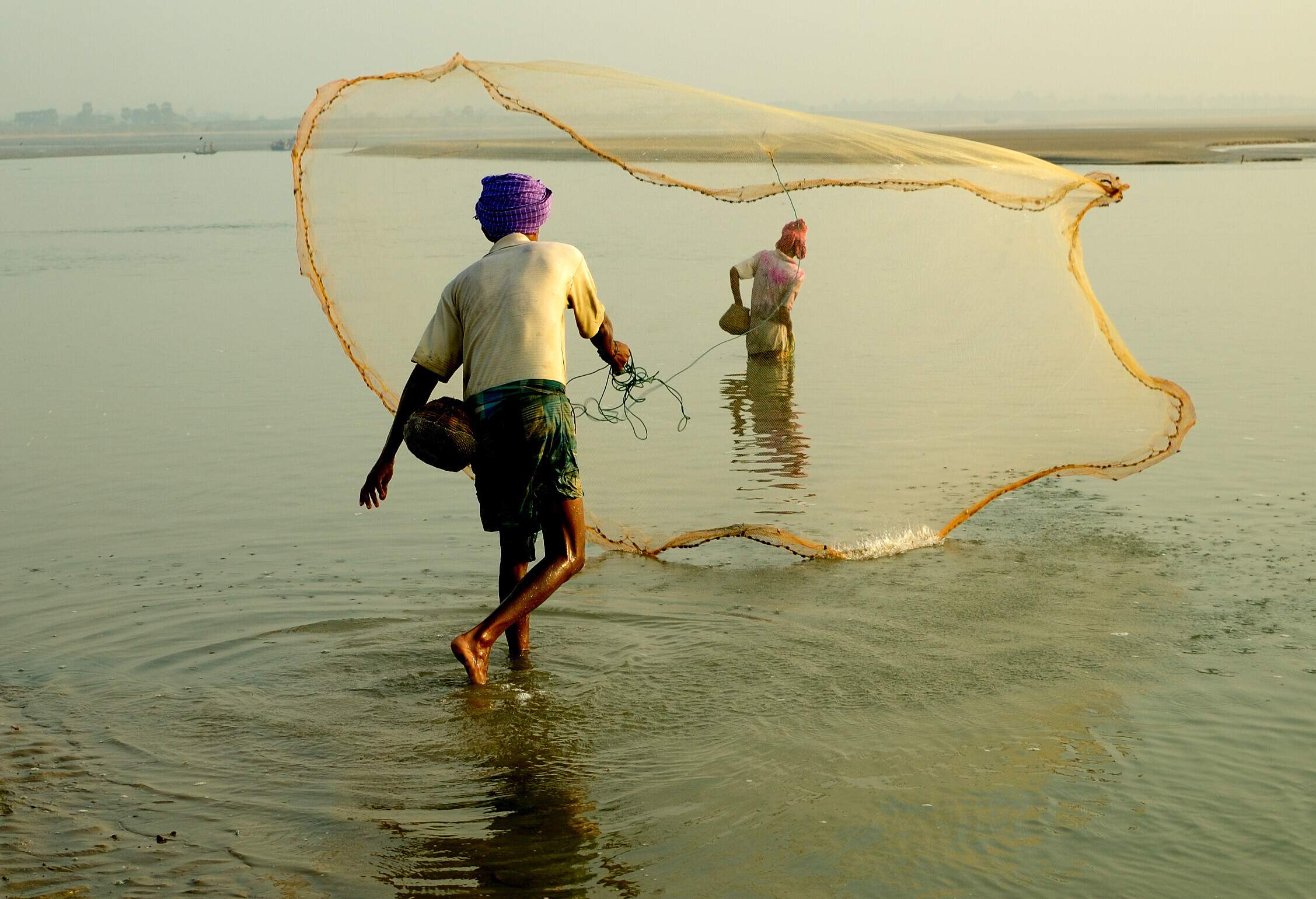 Two people casting a fishing net in the shallows.