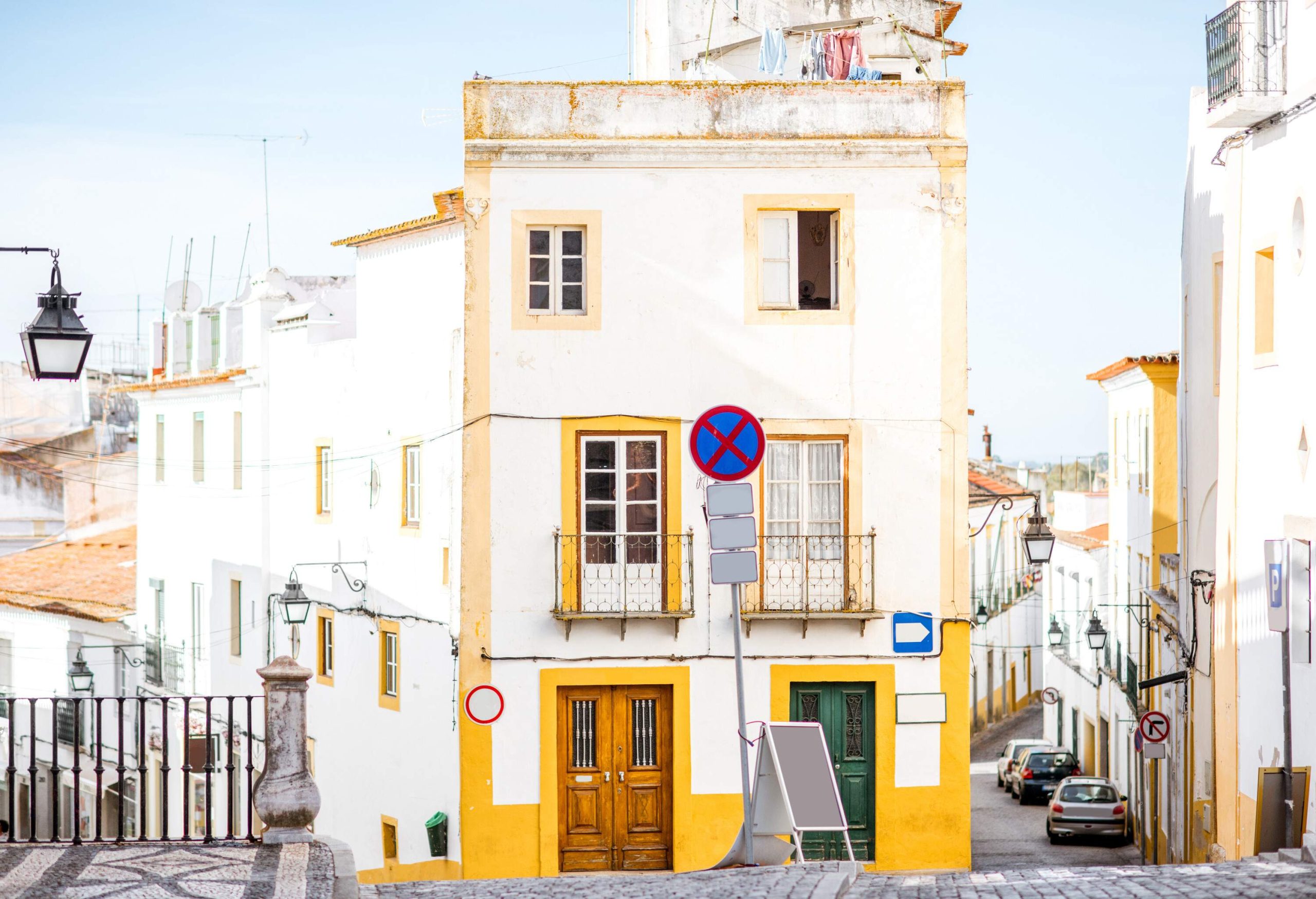 A street along a white building with vibrant yellow door and window frames.