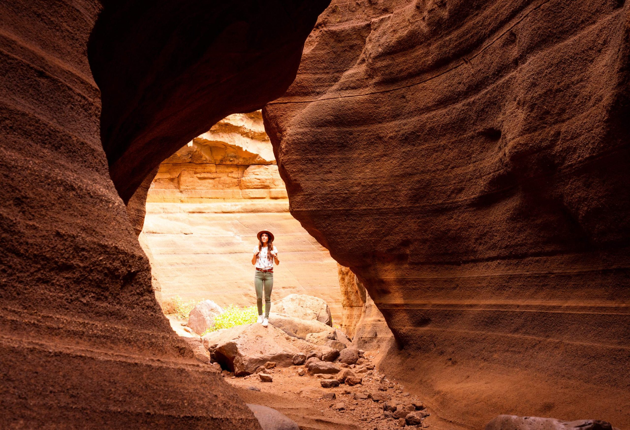 A female hiker wearing a hat standing on a rock in the middle of a canyon.