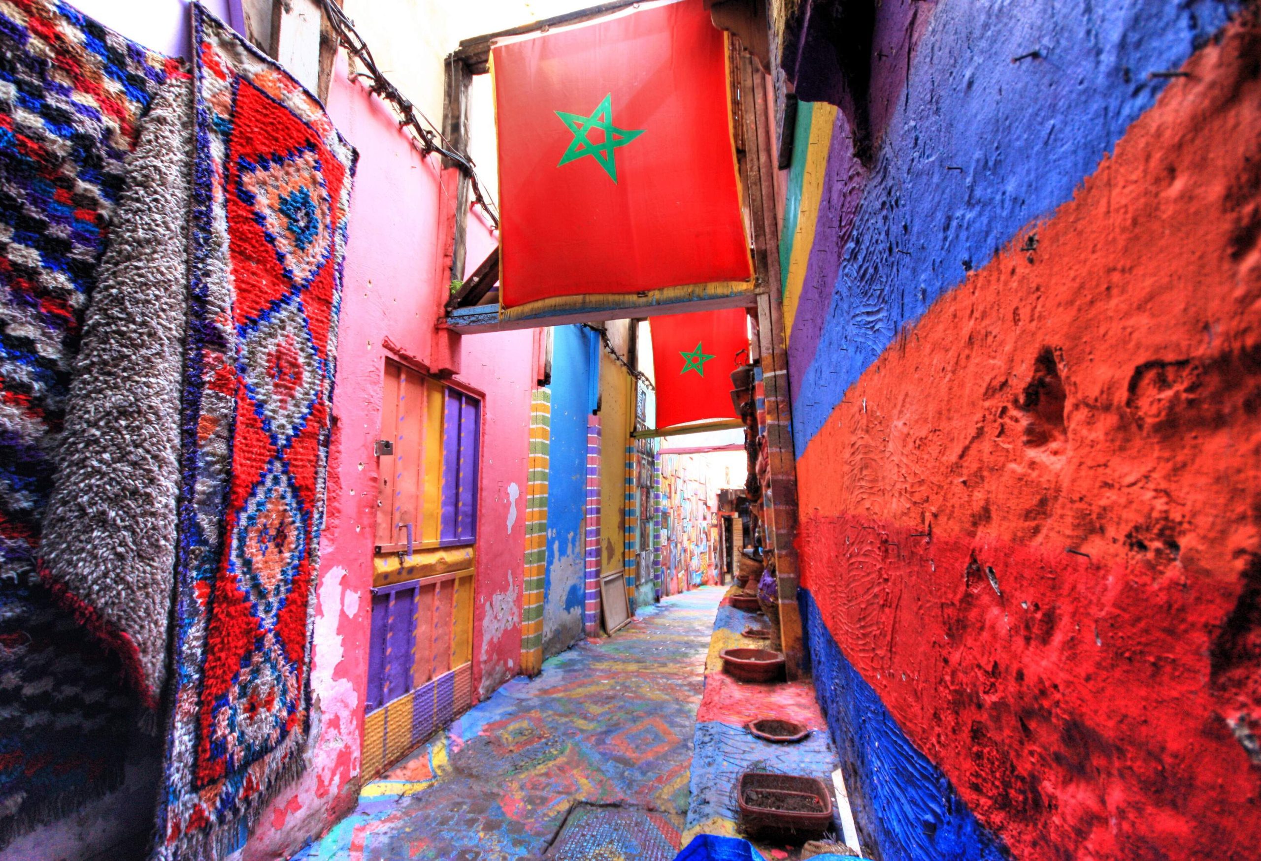 Narrow alley with colourful walls and floors with the Moroccan flag placed overhead.