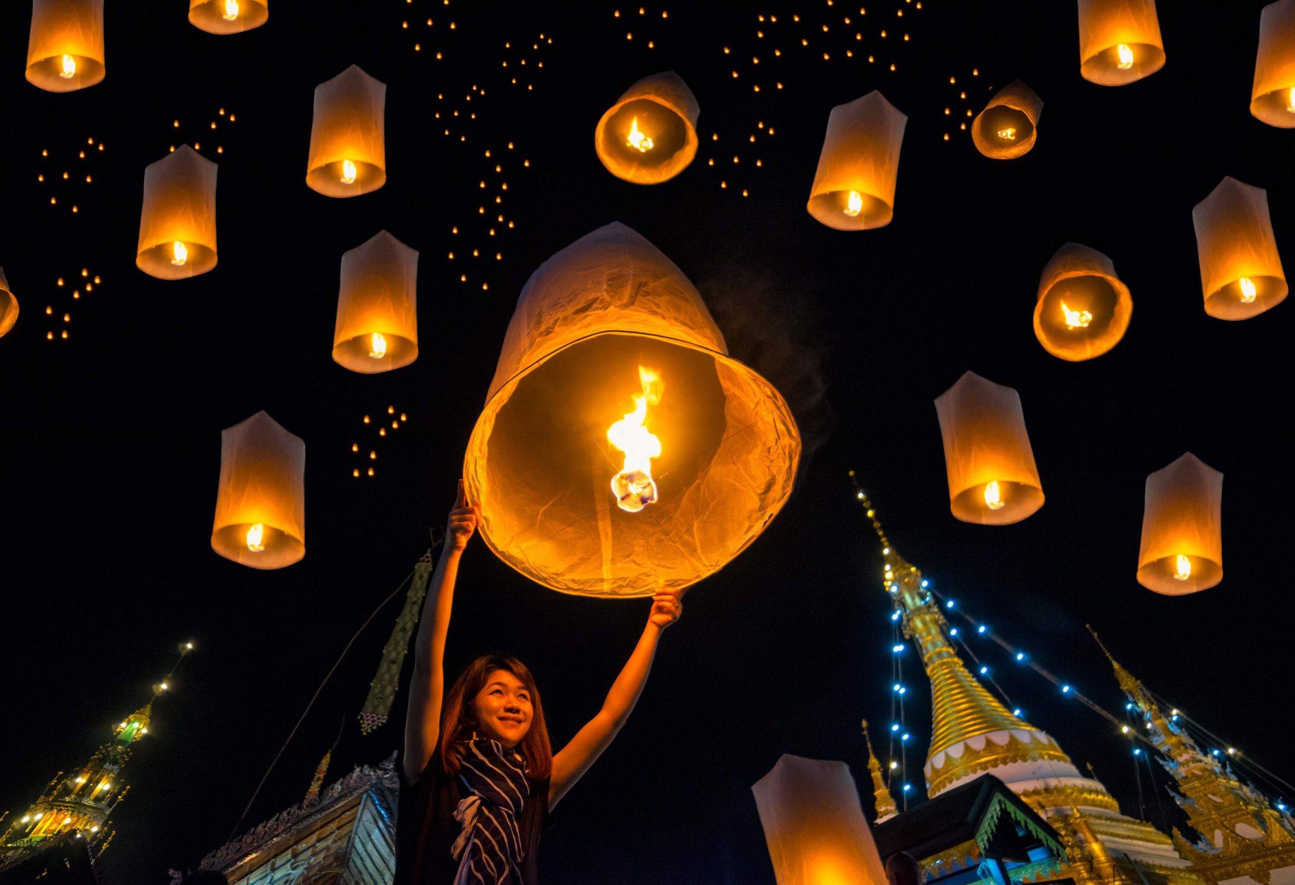 A young woman smiling as she releases a lit paper lantern into the night sky.