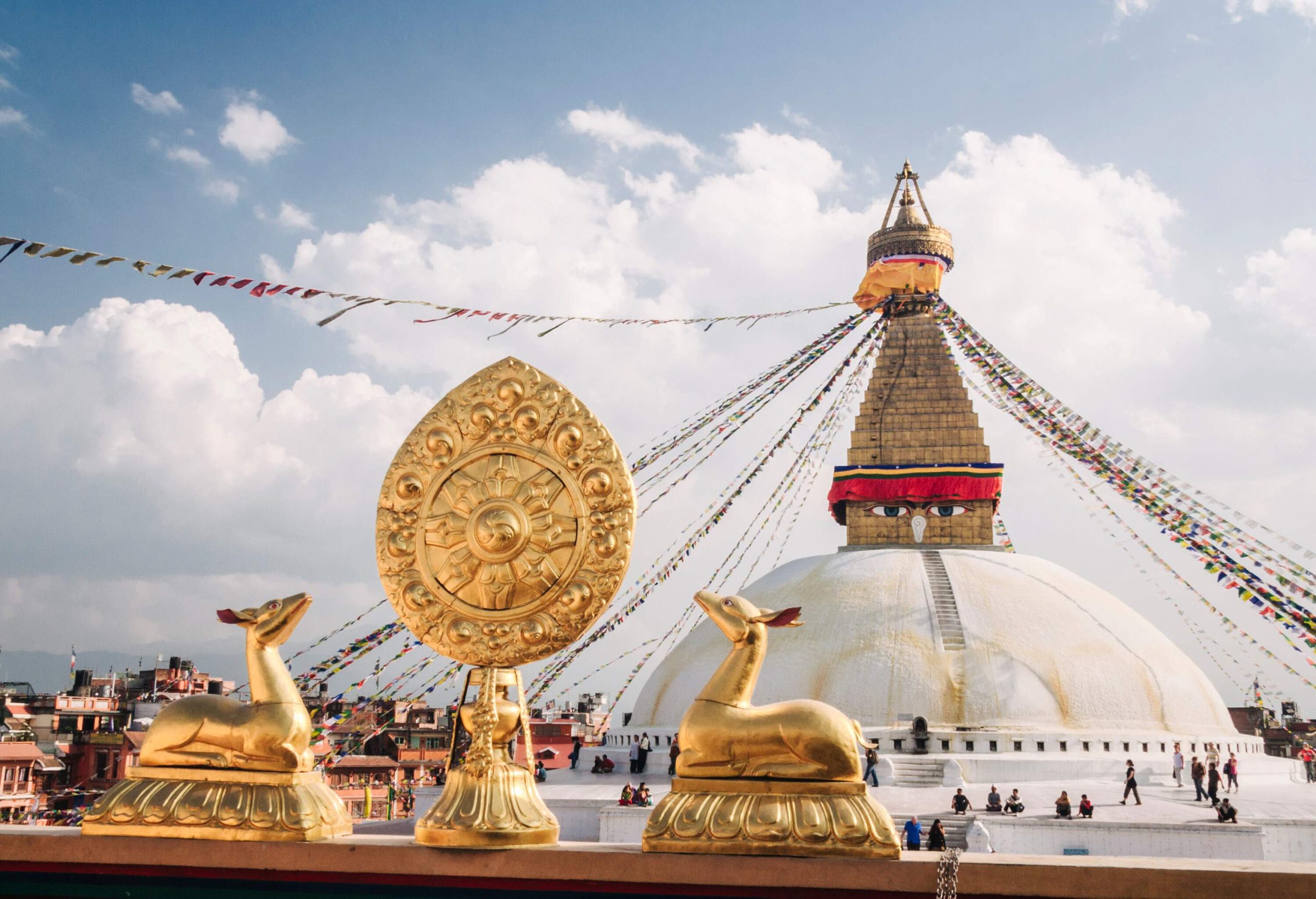 People wandering around a giant stupa decorated with colourful banners and gilded sculptures.