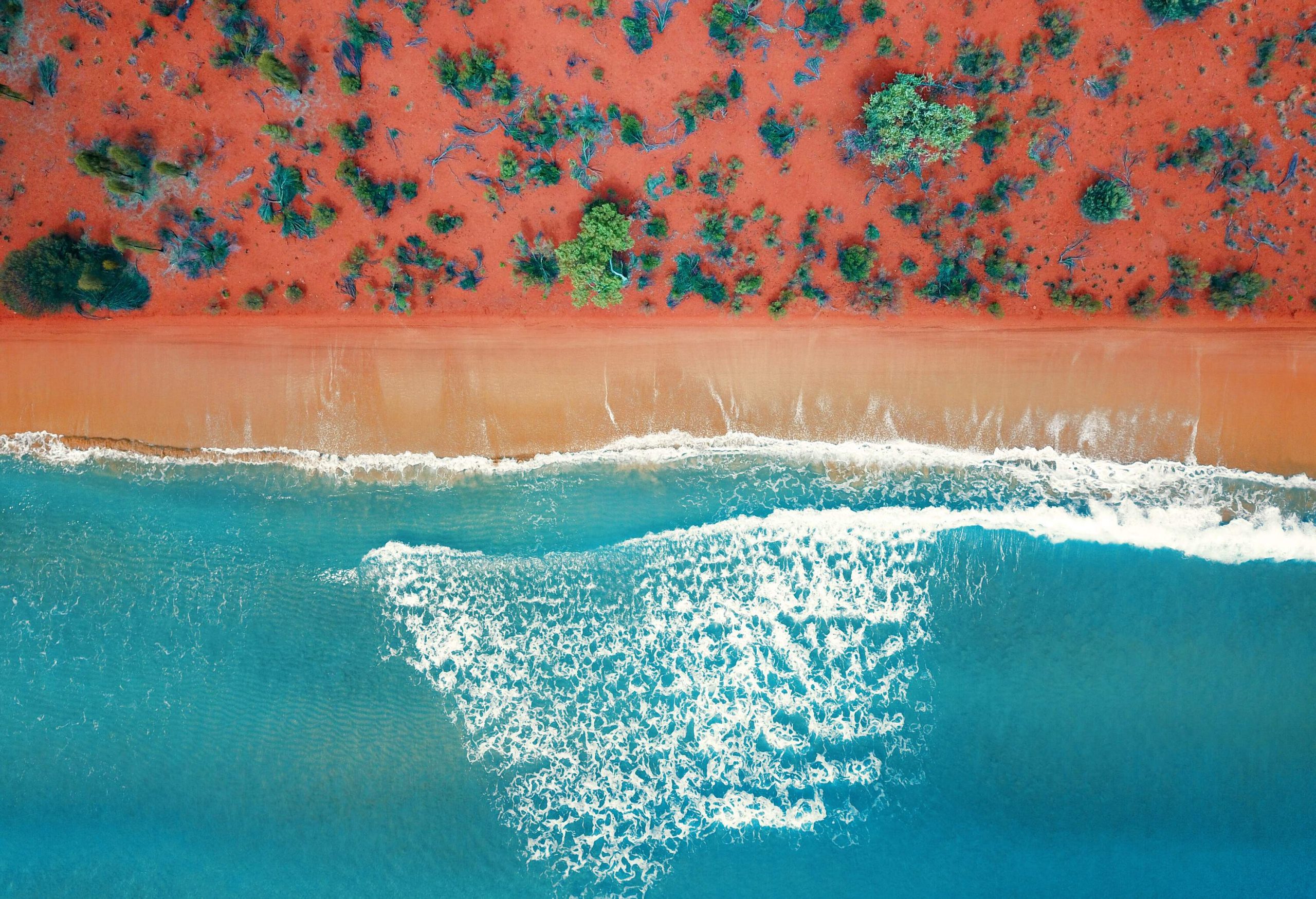 Top view of orangy sandy shore by the wavy turquoise sea.
