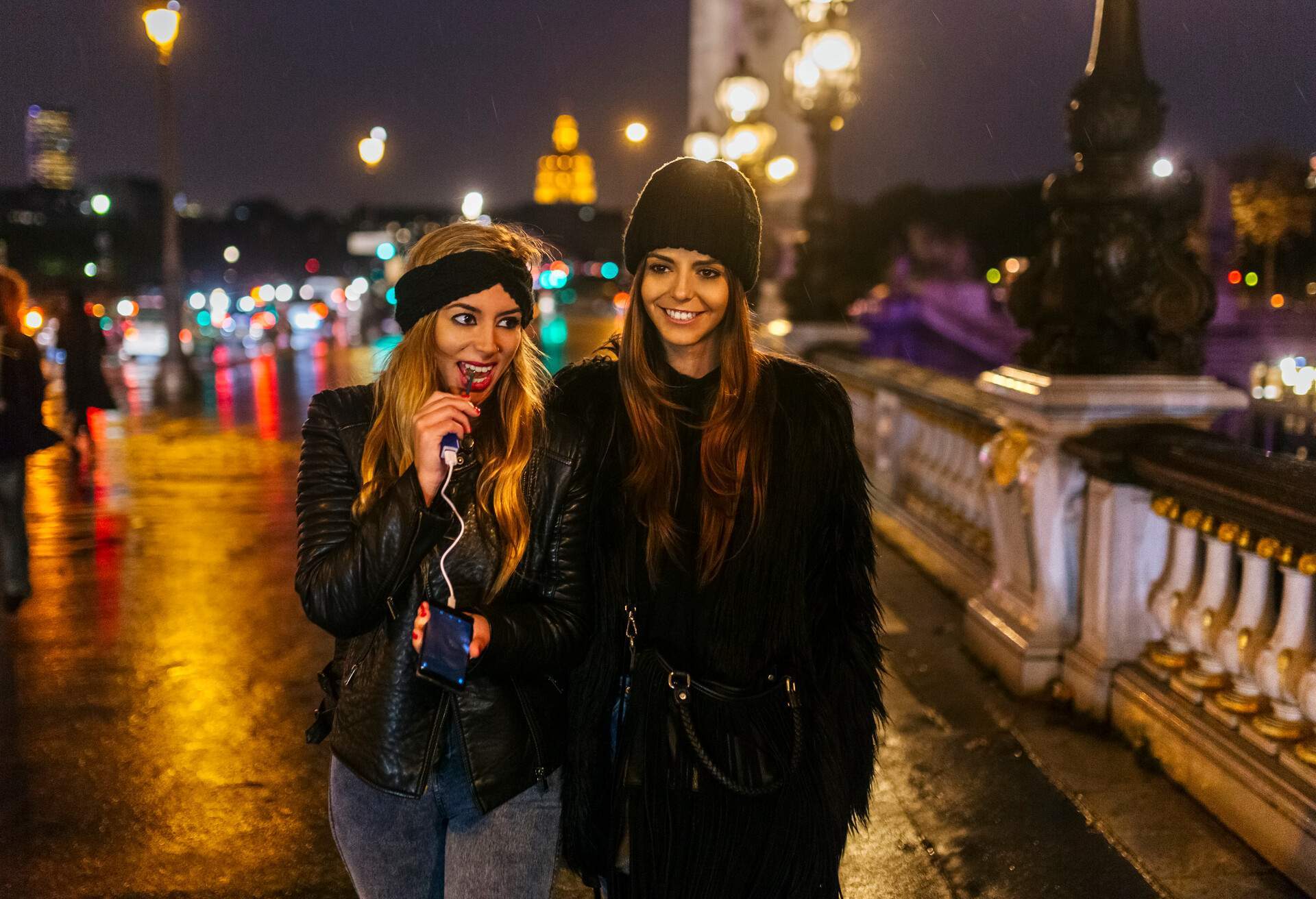 Two female friends standing on a bridge on a rainy night.