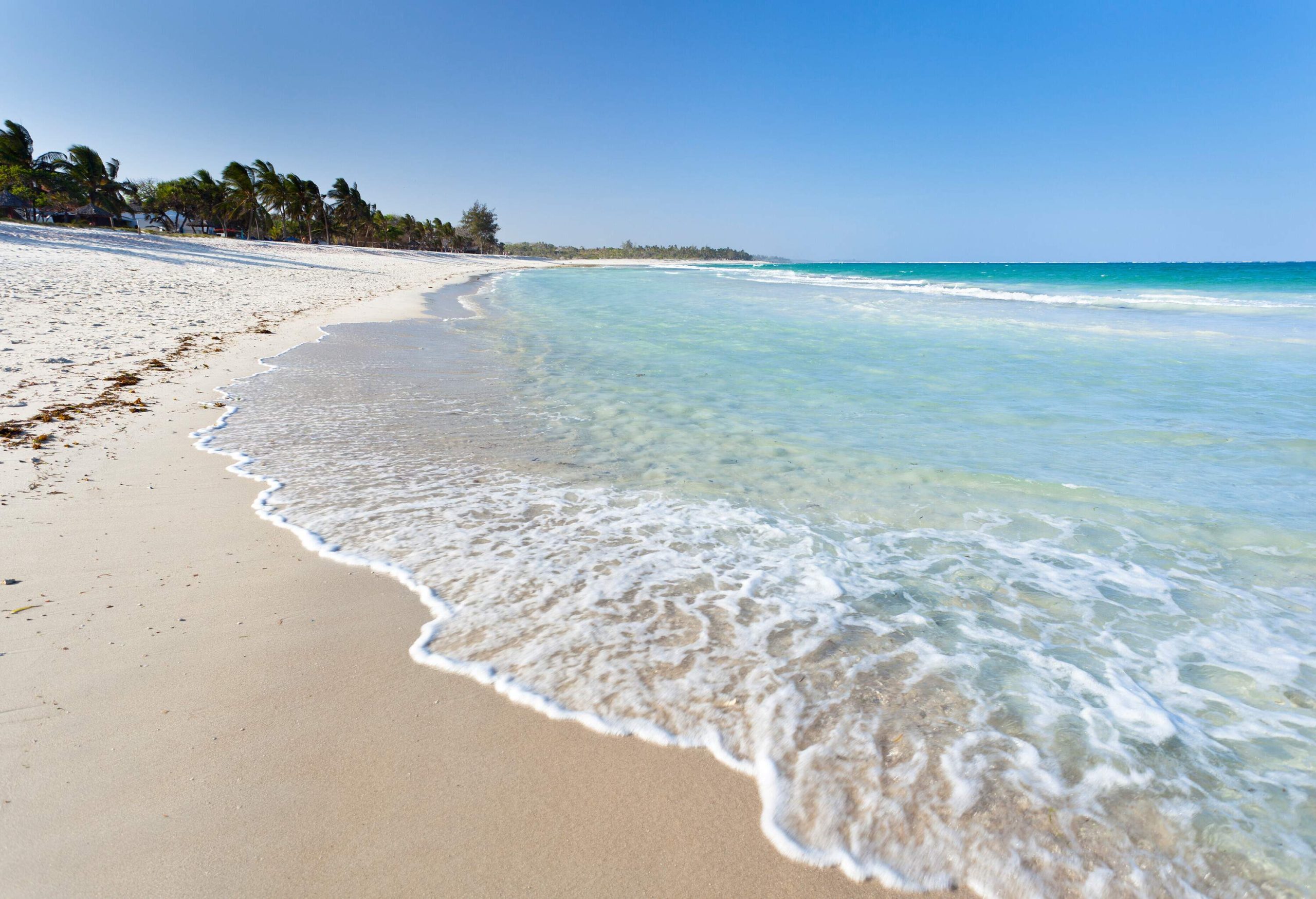 A white sand beach with gentle waves and distant views of palm trees.