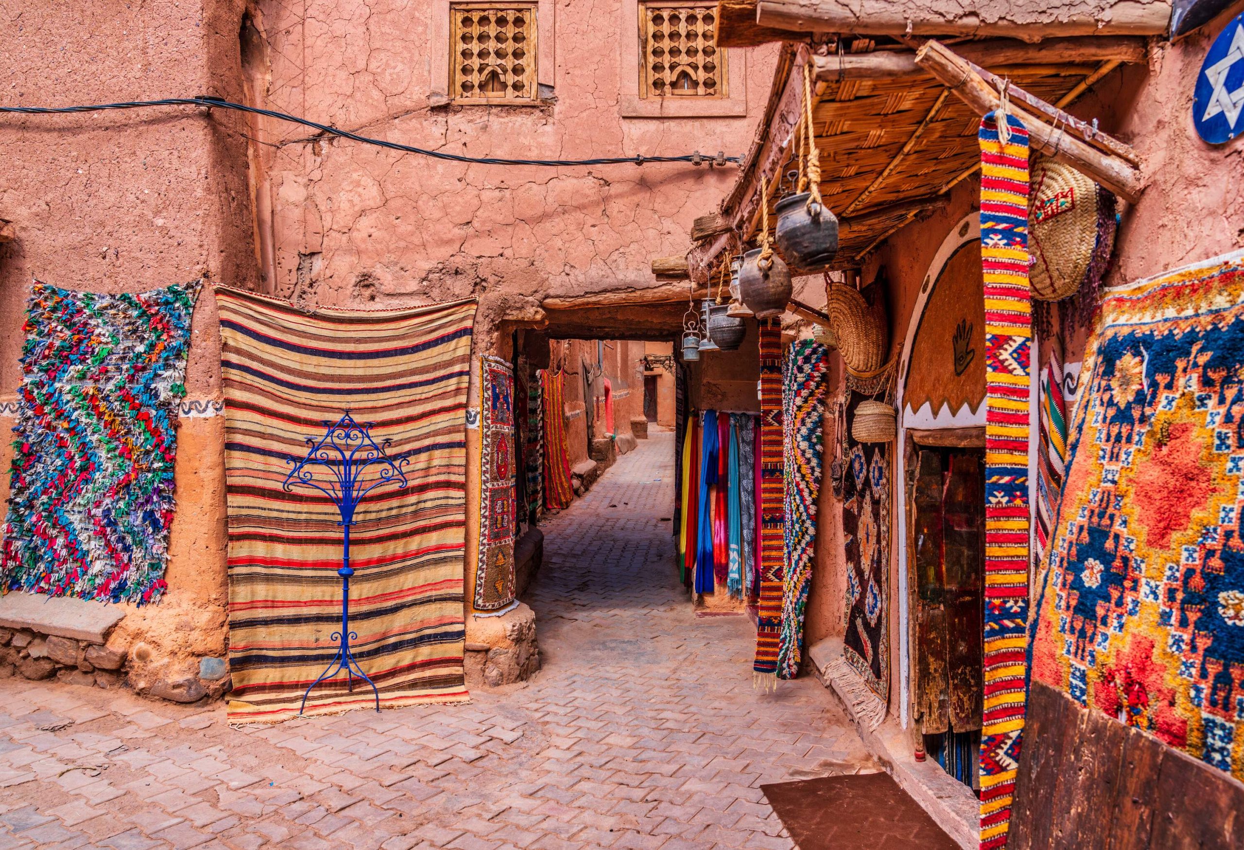 A narrow street inside a compound with colourful handmade carpets and rugs hanging outside the traditional houses.