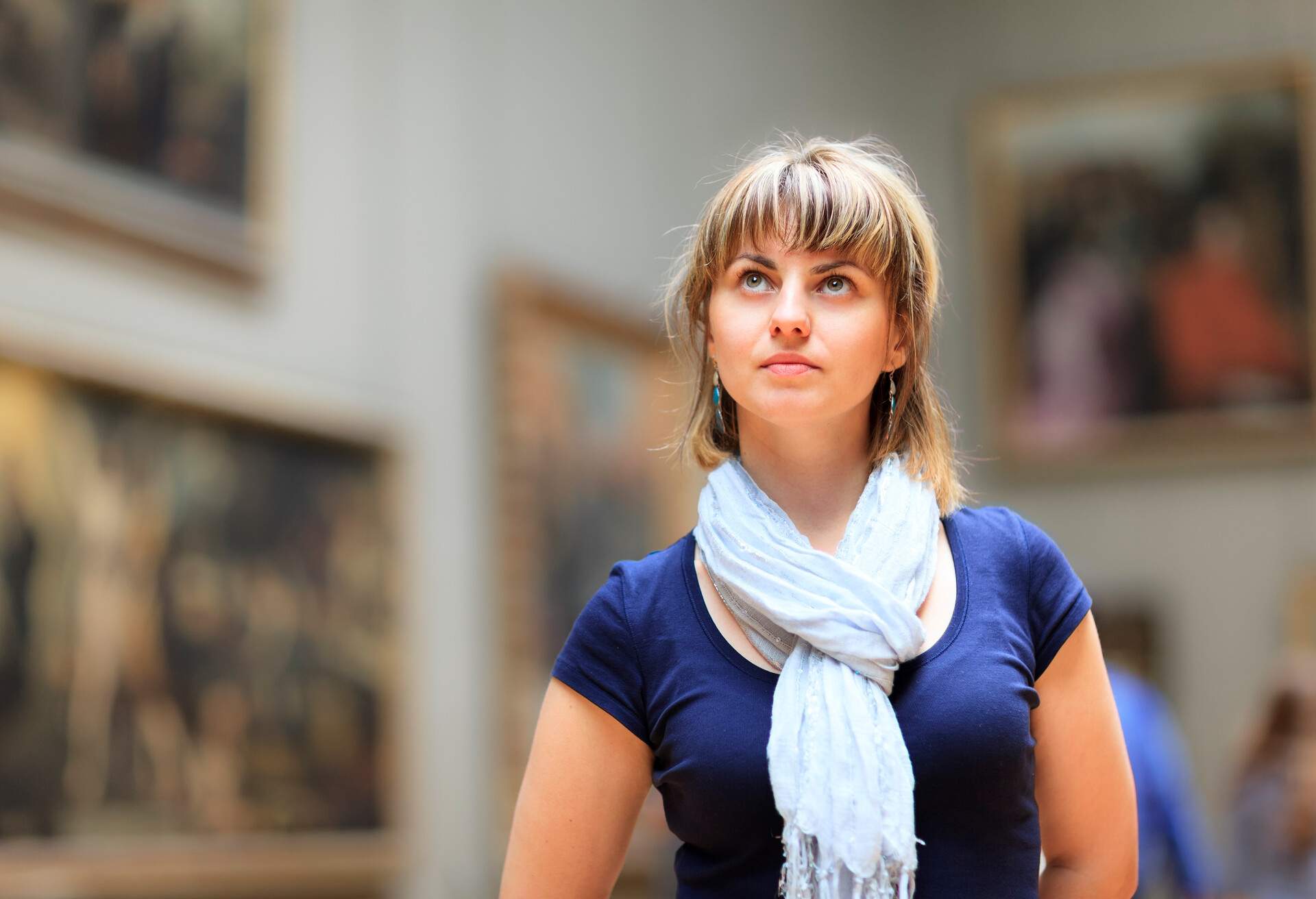 Brunette in a navy shirt and white scarf looks up.