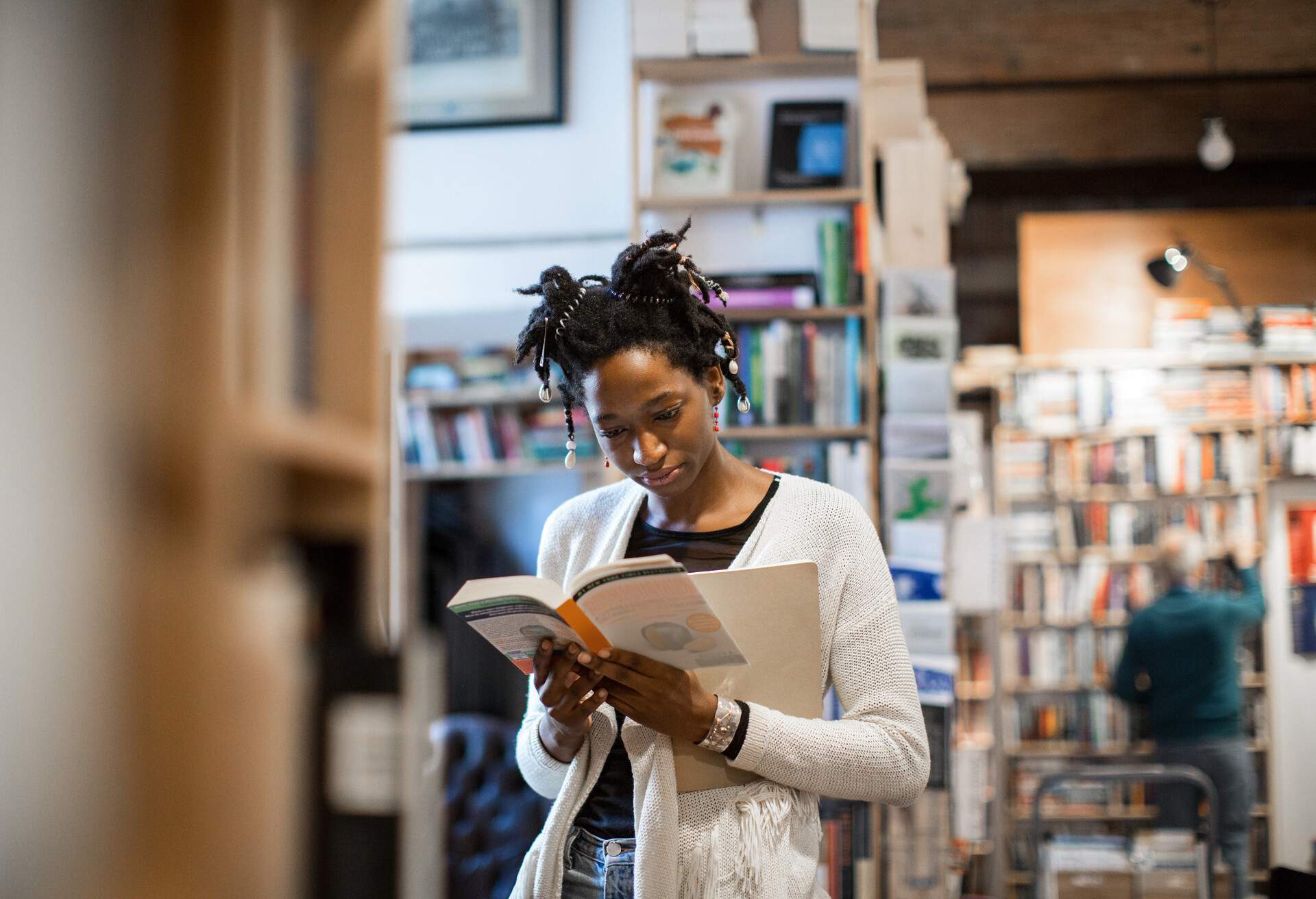 Young female customer reading book while standing in bookstore 