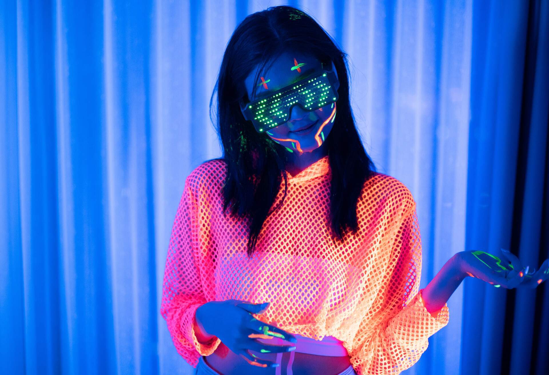 Ultraviolet lights illuminate a woman wearing neon orange clothing, LED sunglasses, and face paint.