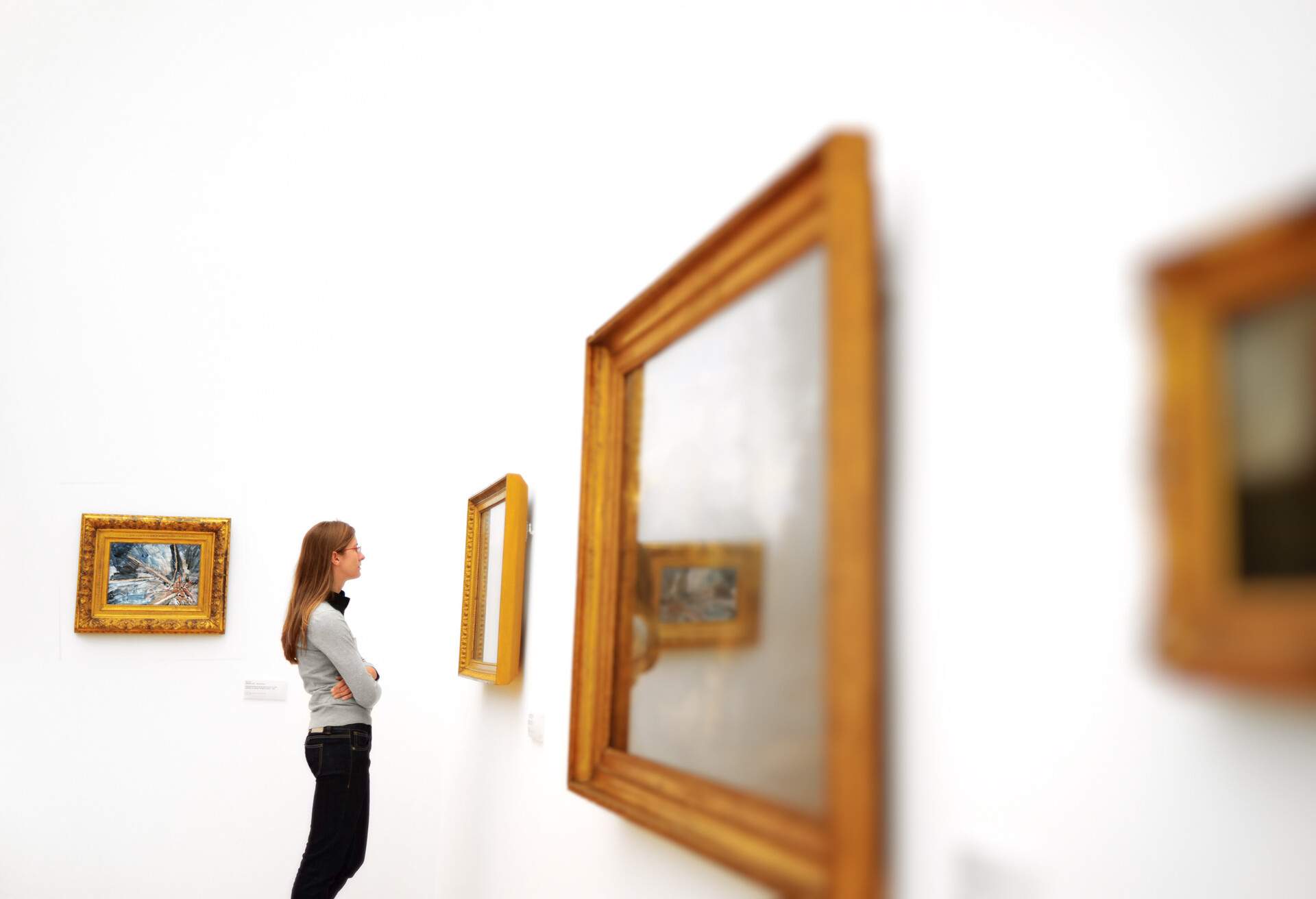 A young woman standing with arms folded over her chest admiring wooden framed wall art.