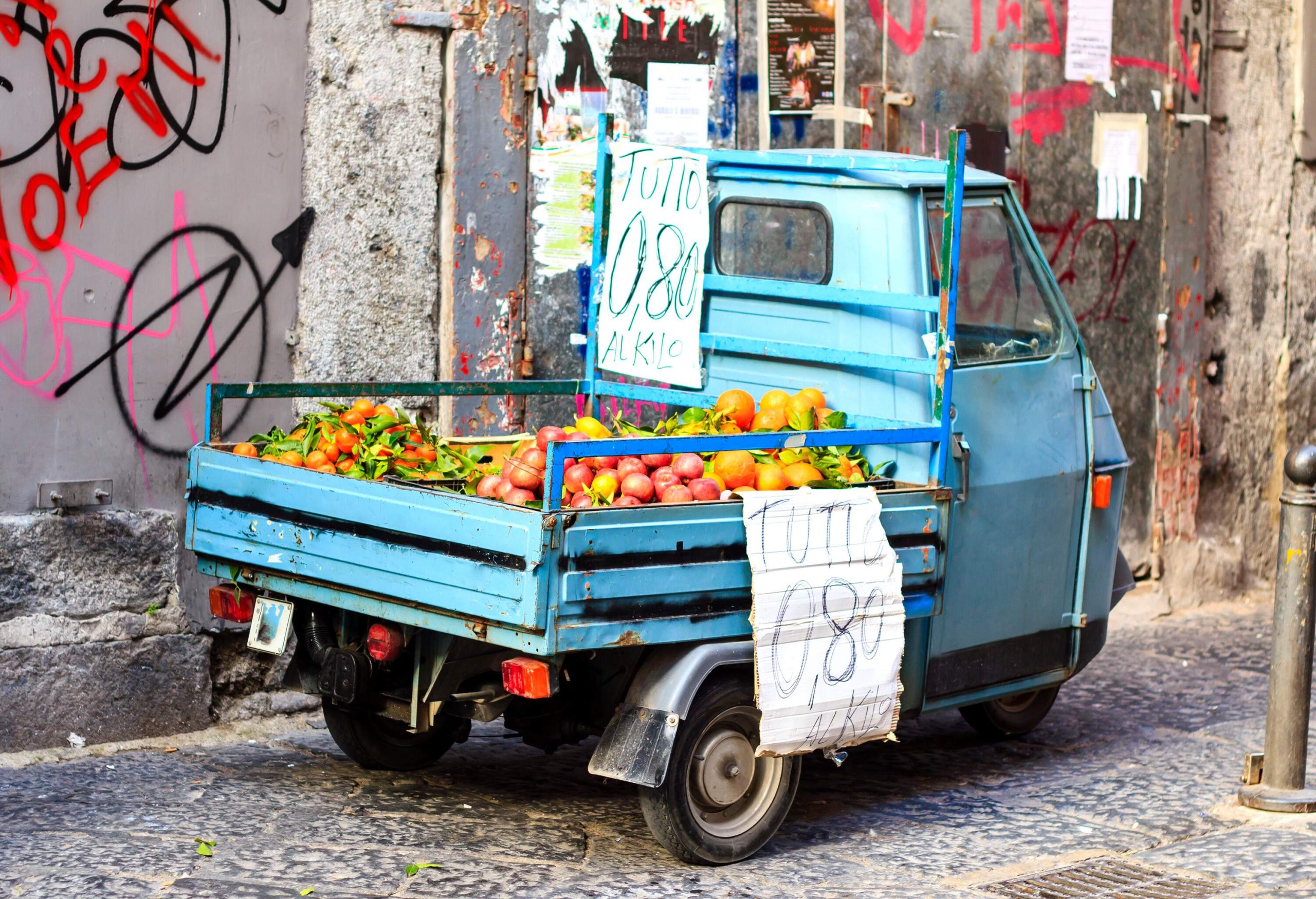 A sky blue mini truck with loads of fruits for sale.