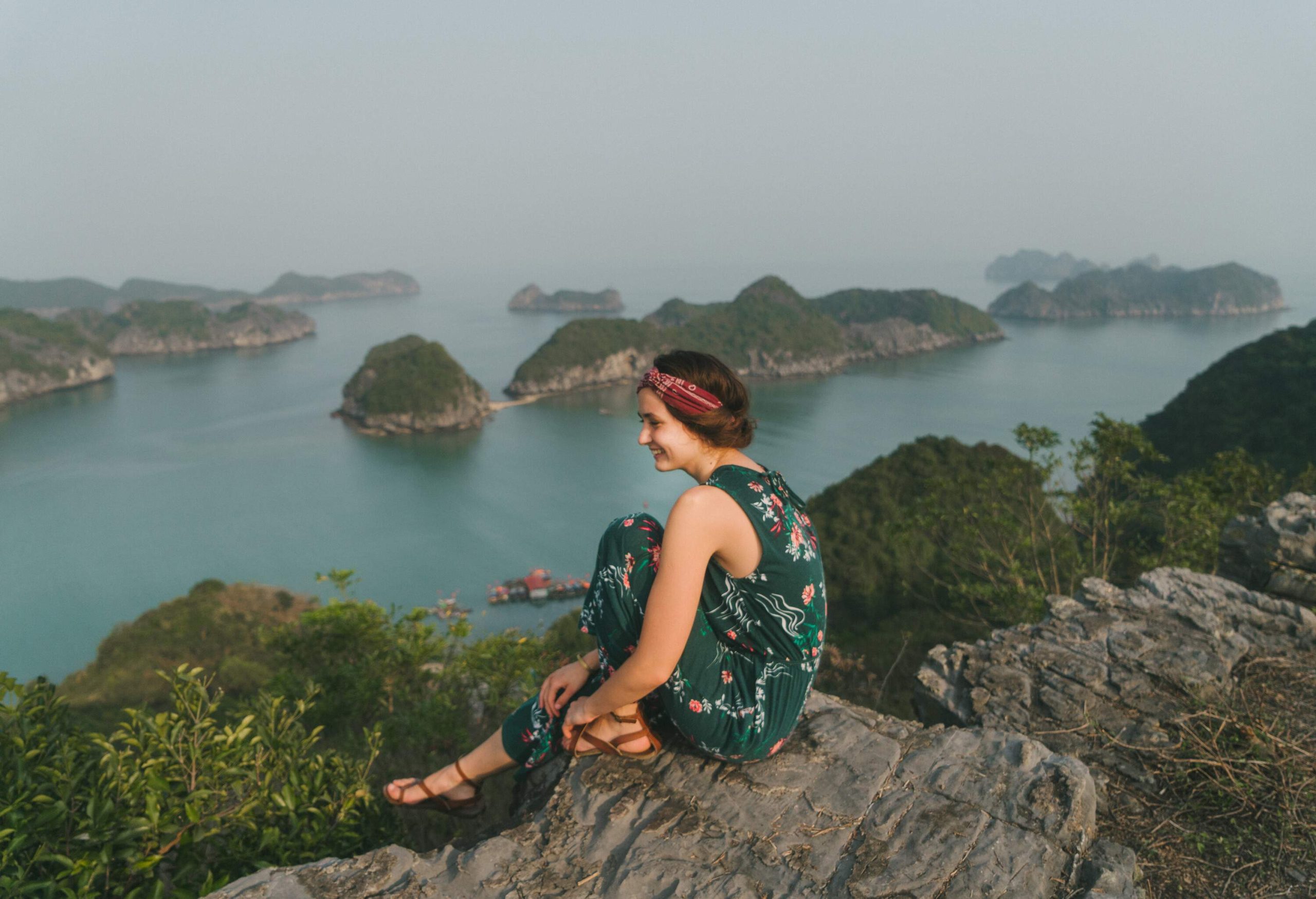 An individual on a cliff overlooking the breathtaking towering rock limestone islands topped by rainforests, surrounded by the majestic turquoise sea.
