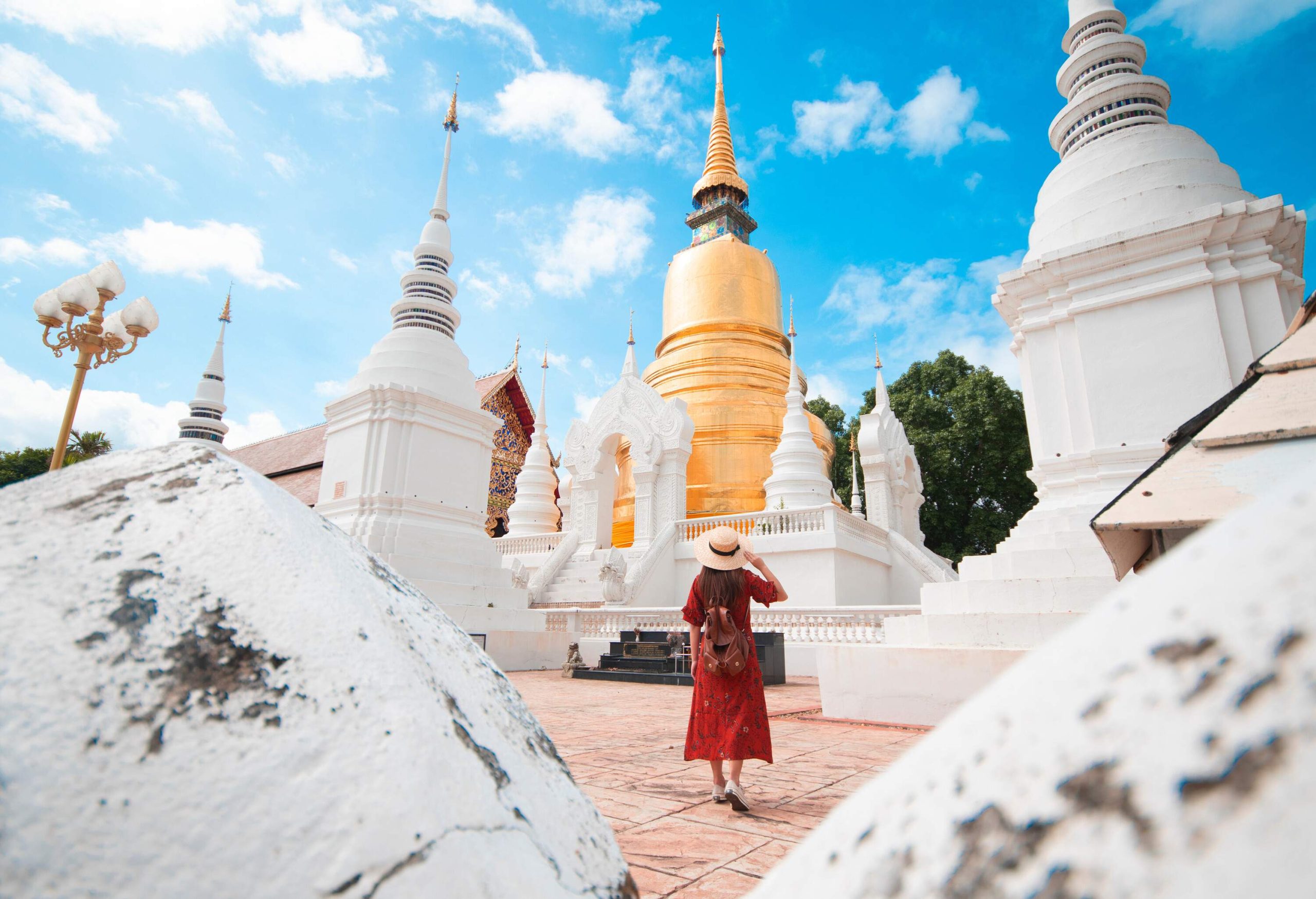 A female tourist in a red dress and a hat walking across a Buddhist temple.