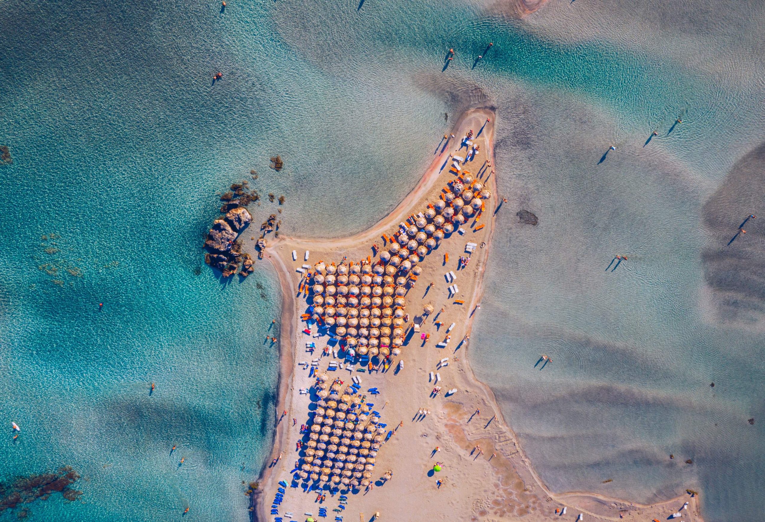 A crowded pink sand beach with a cluster of sunbeds and umbrellas.