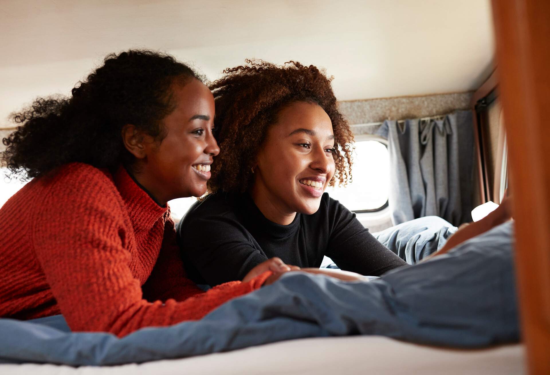 Happy female friends taking selfie while lying on bed in camper van during vacation 