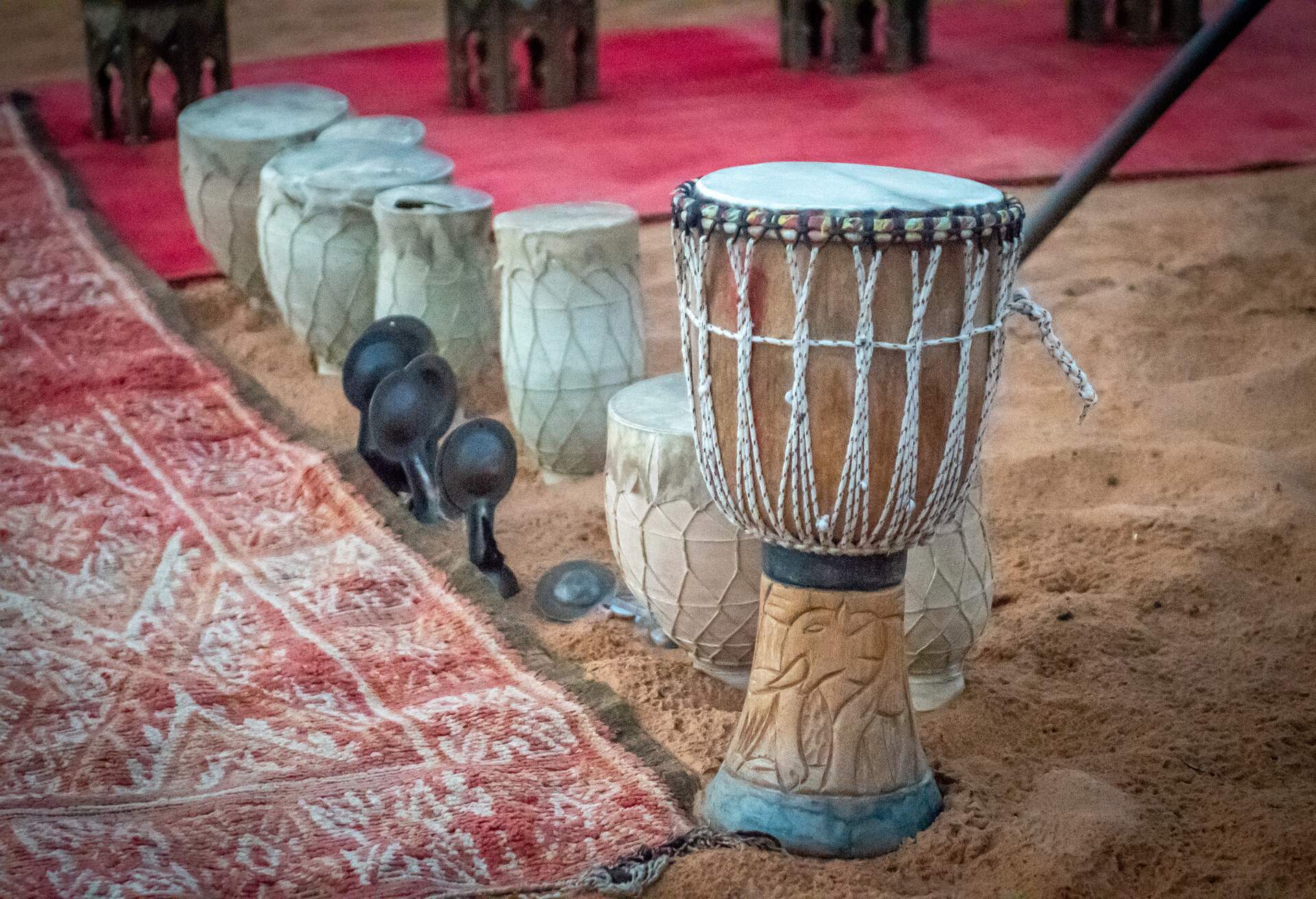 Traditional Moroccan drums line on the sand along a red tessellated carpet.