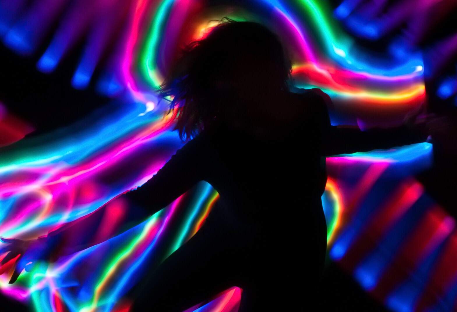 Silhouette of a person dancing against the streak of colourful neon lights.
