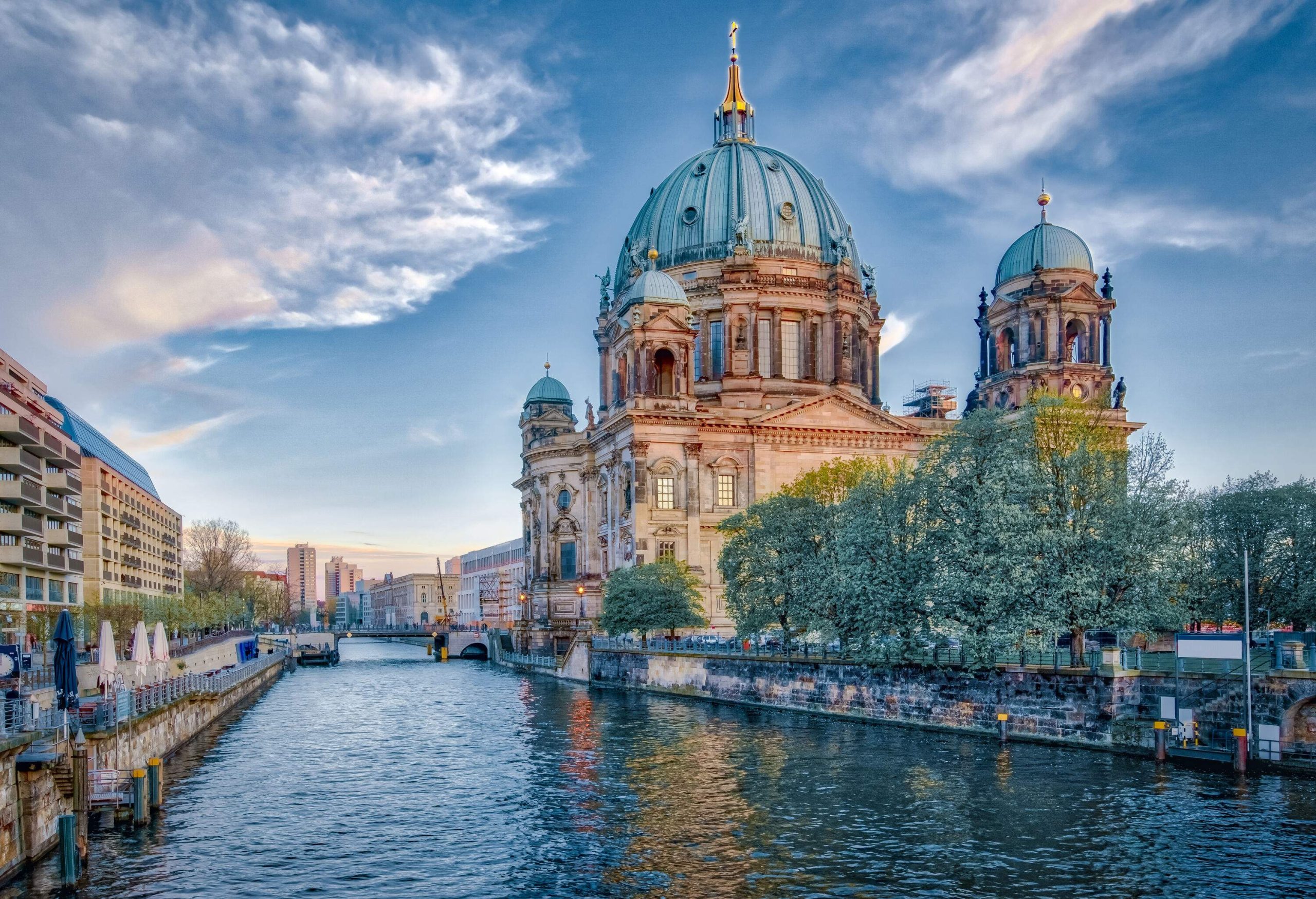 The beautiful palace-like Berlin Cathedral on the riverbank with dramatic blue sky.