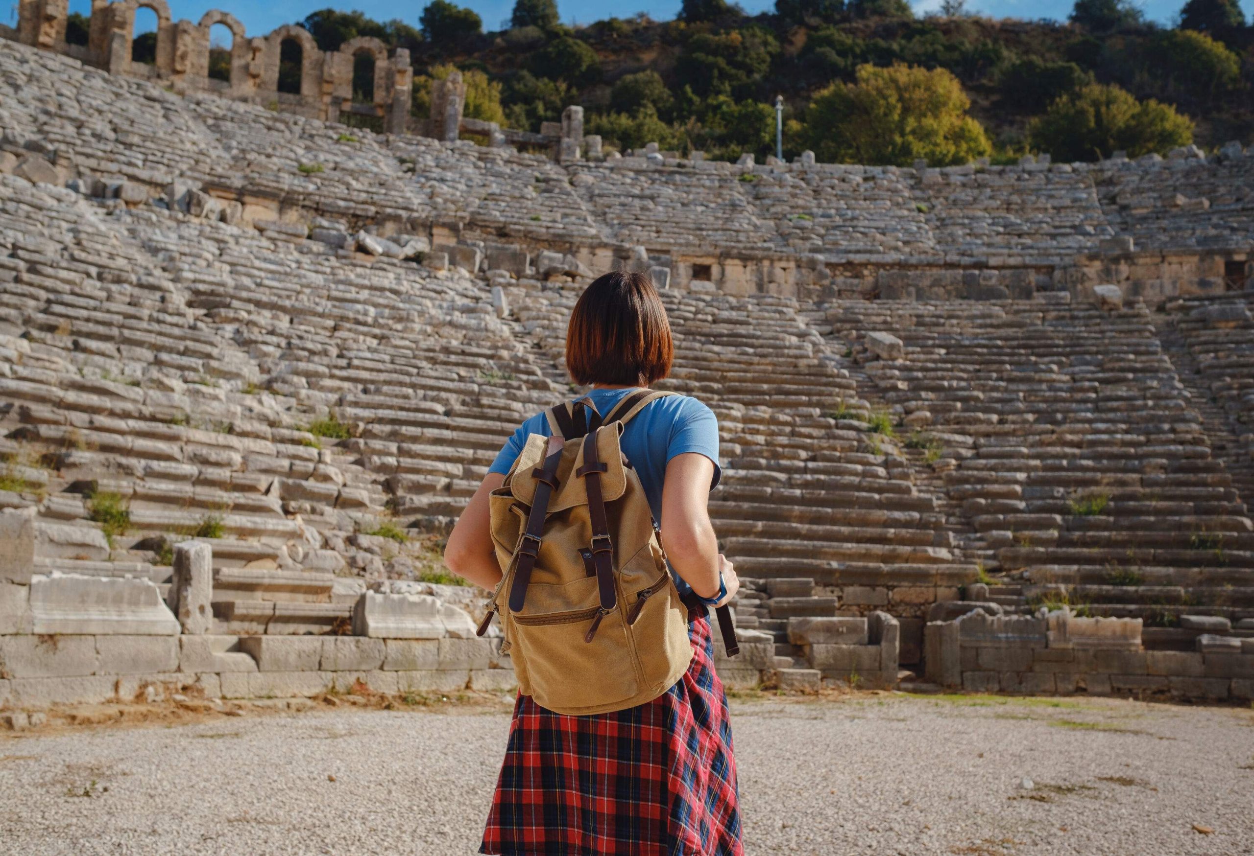 An individual stands in the centre of a ruined ancient theatre.