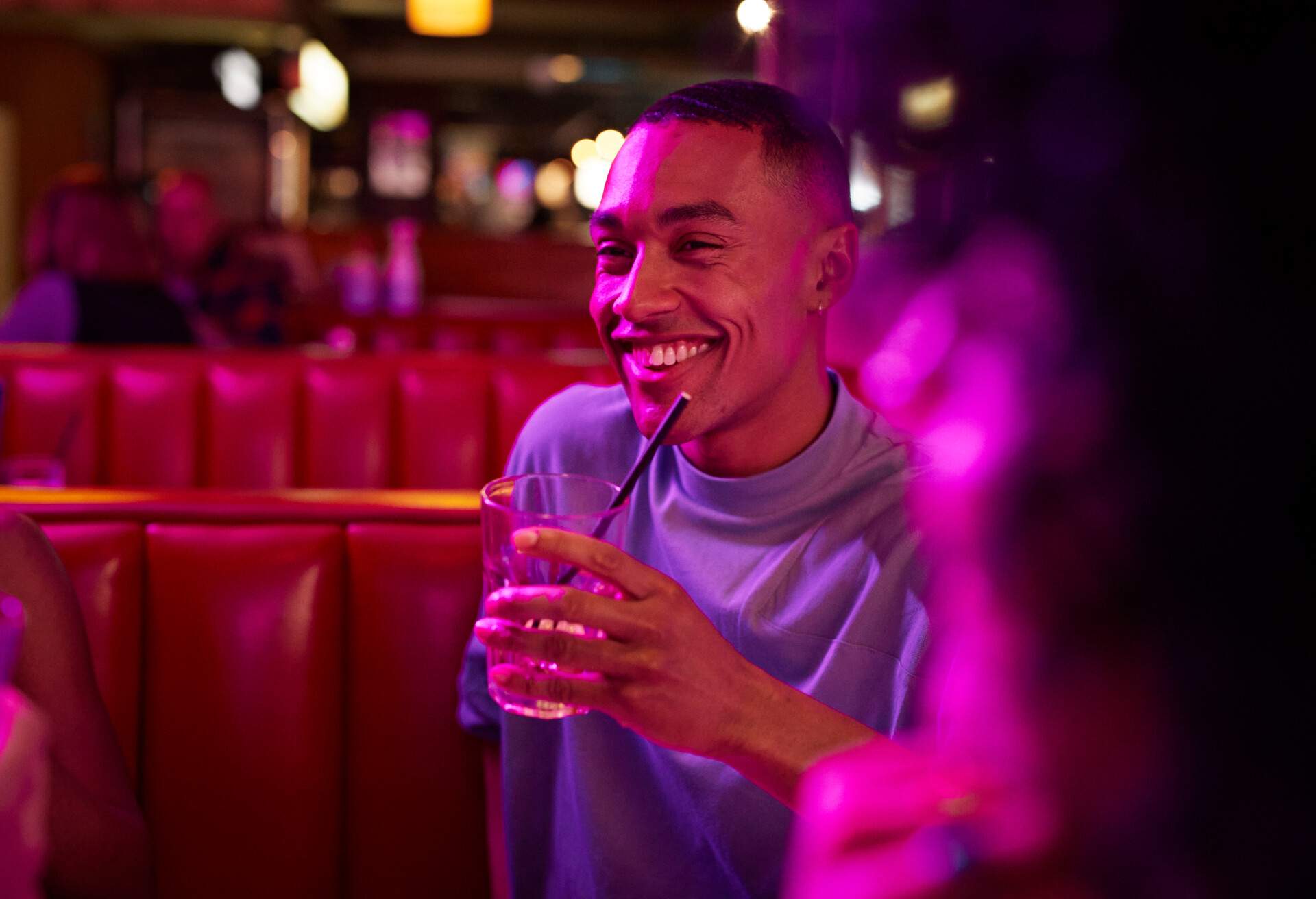 A man seated in a booth, holding a drink and smiling.