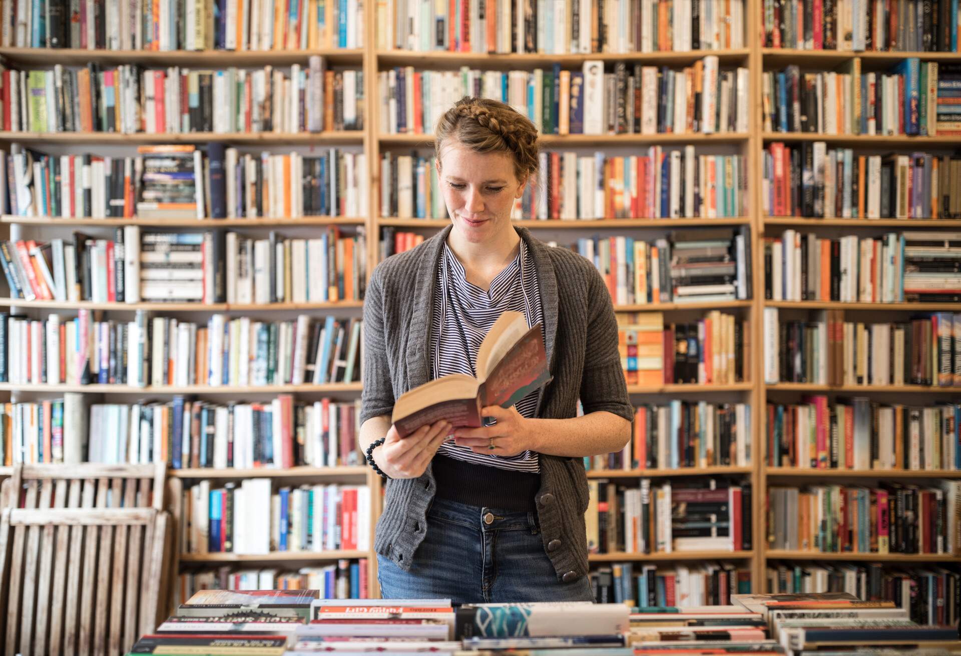 Woman reads a book while standing against bookshelf in bookstore.