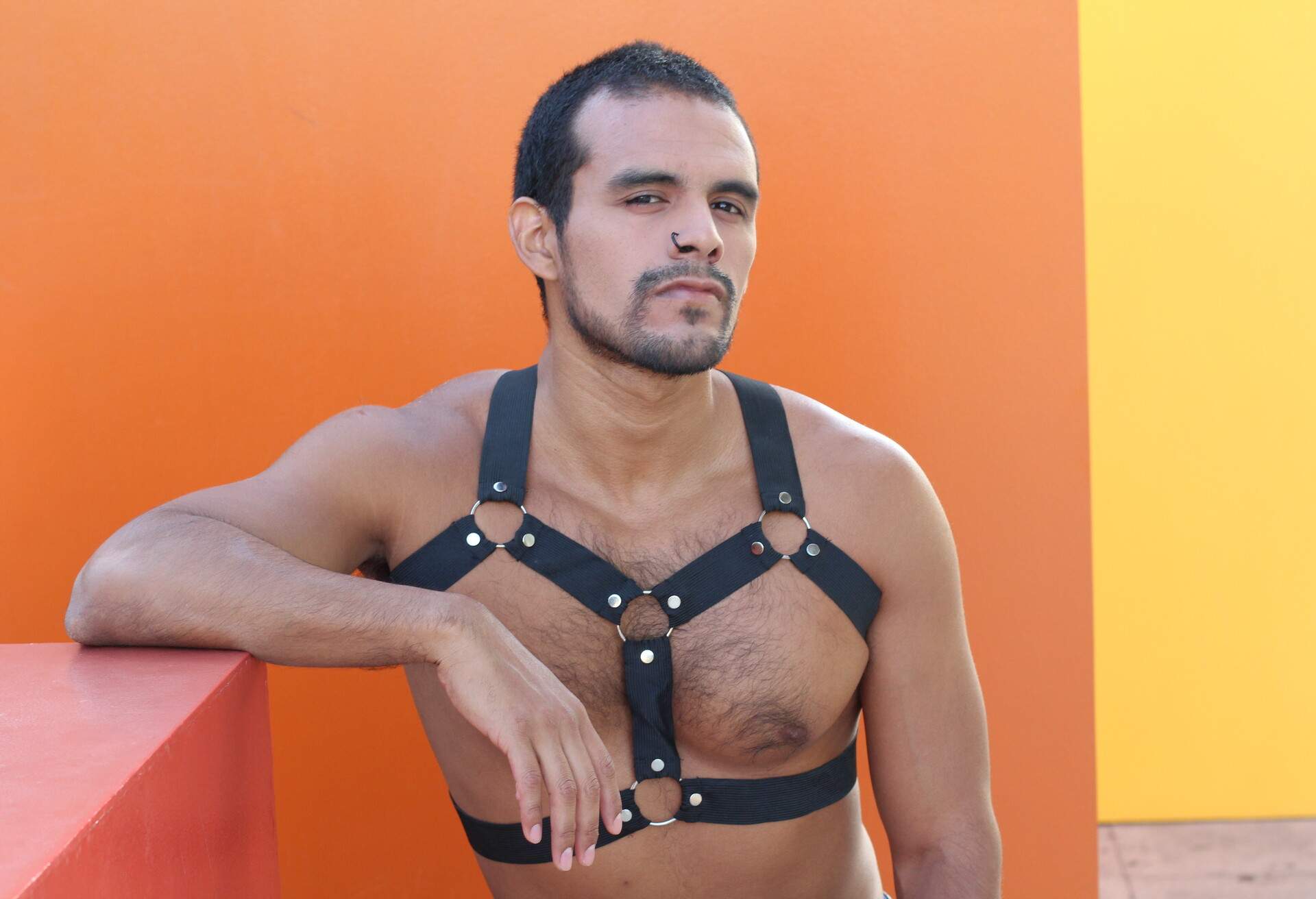 A man wearing a chest harness standing against an orange wall.