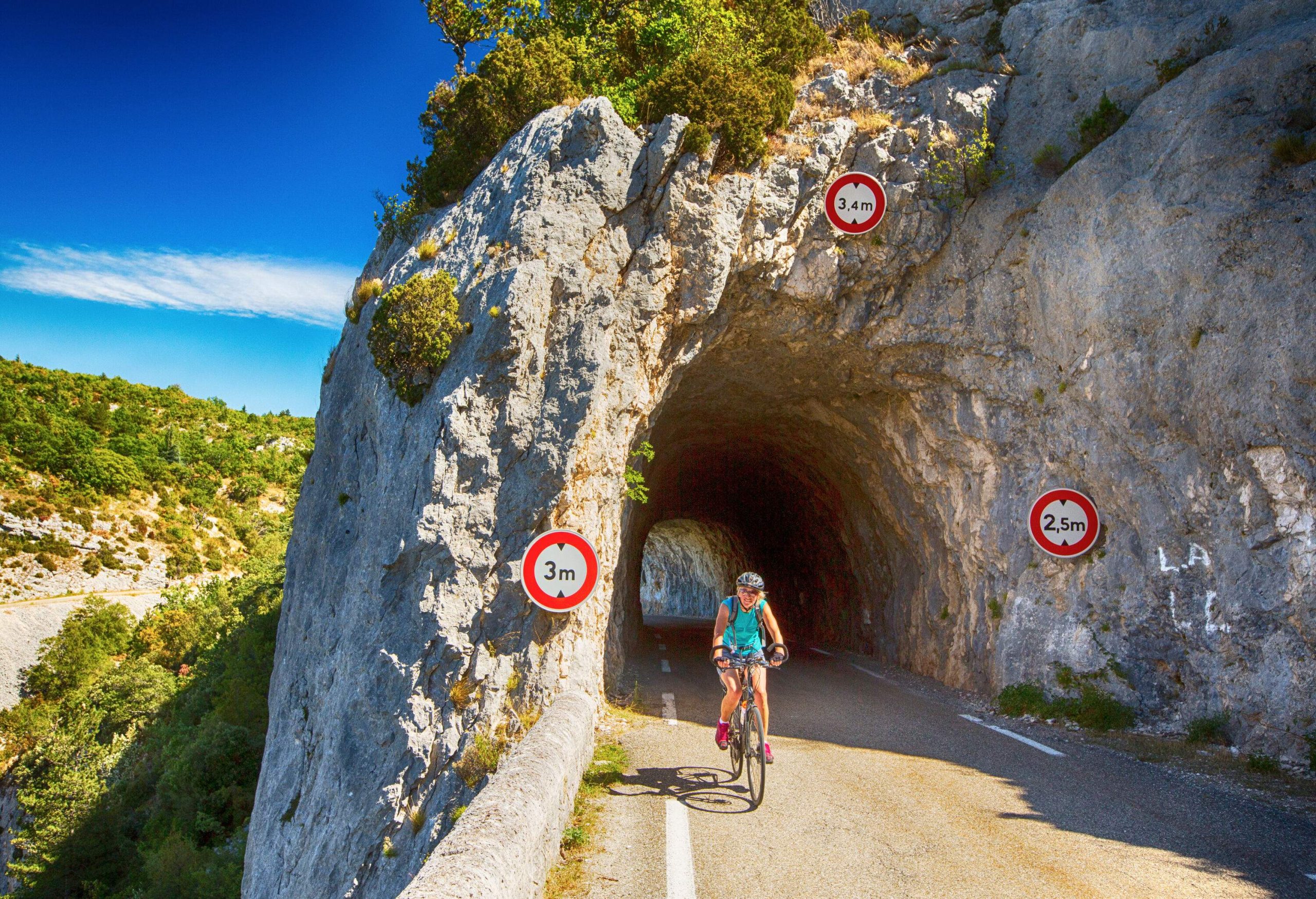 A woman biking pass through a cave road on the mountainside.