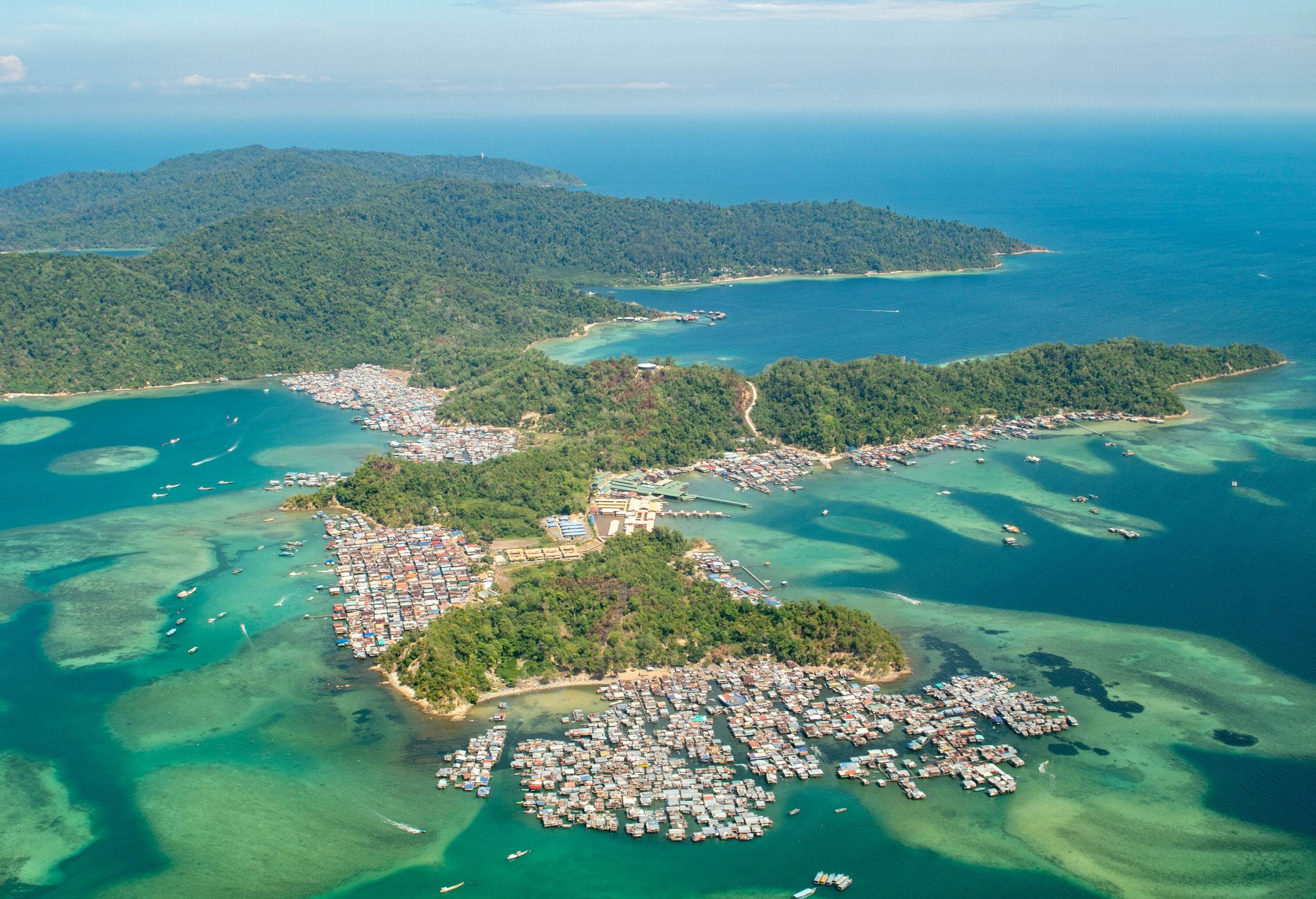 A forested island with a coastal village featuring a cluster of homes perched on stilts.