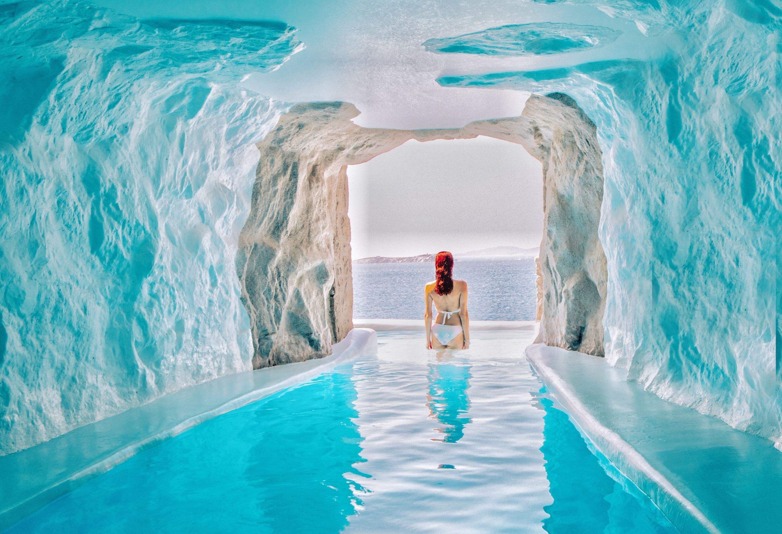 A woman in a bikini stands at the entrance of a cave pool with white painted walls and ceiling.